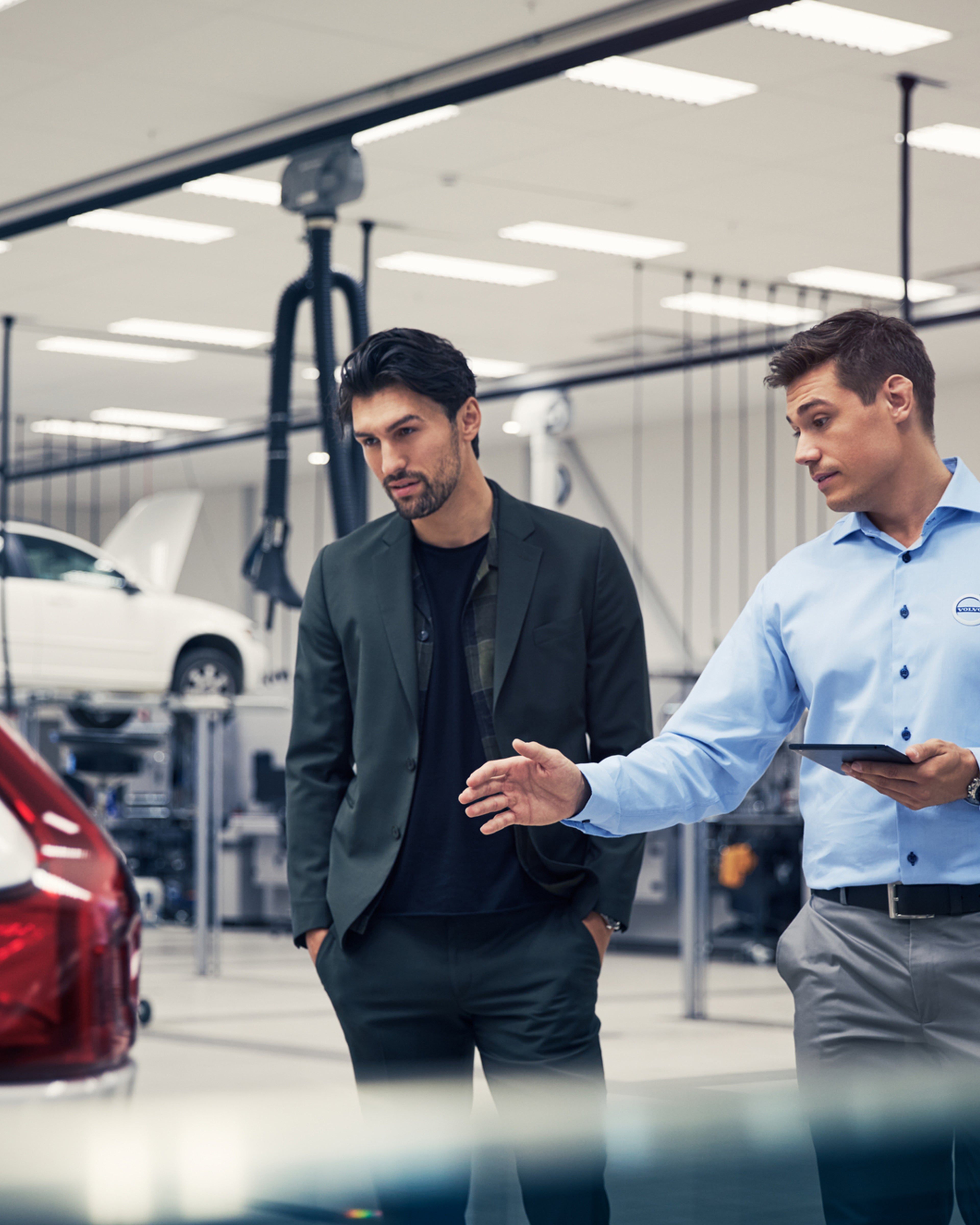 Volvoansatt peker på bil med nettbrett i hånden mens han snakker med eieren