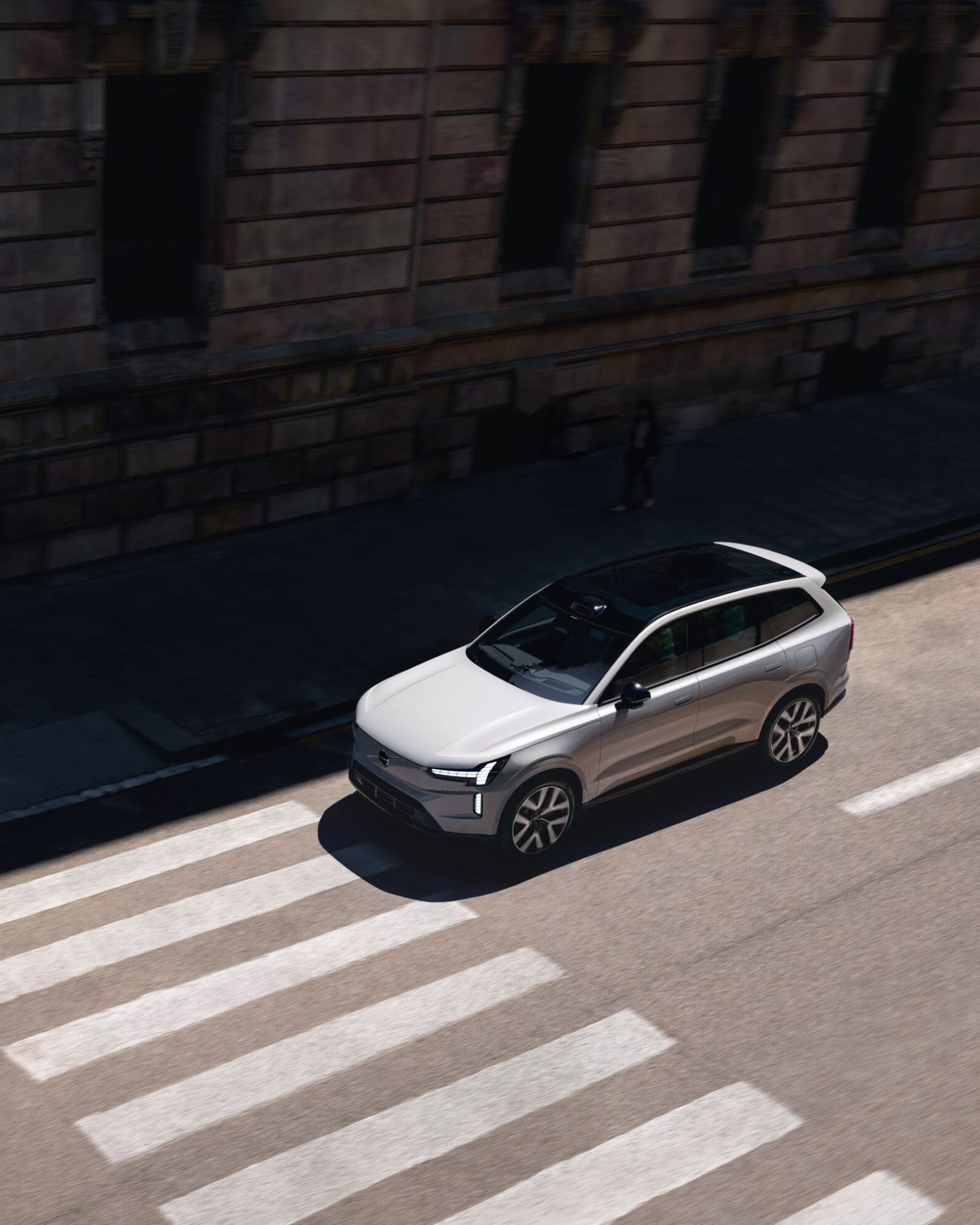 Een zilvergrijze Volvo EX90 elektrische SUV rijdt onder op de weg, vogelperspectief