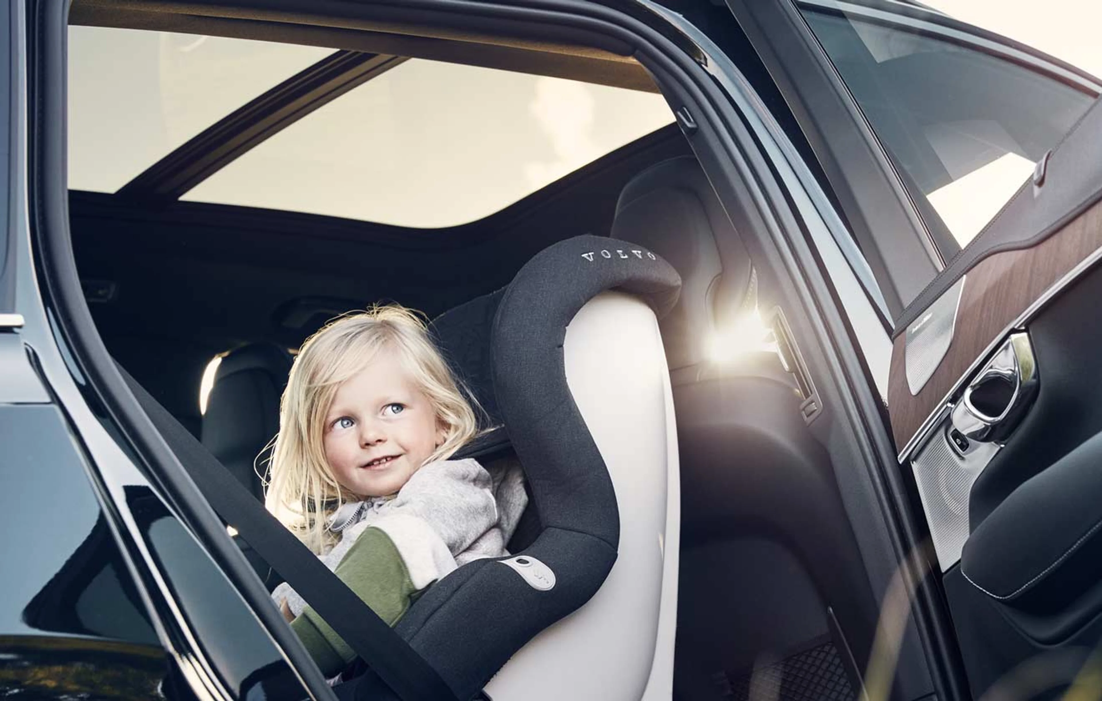 Enfant assis dans un siège auto Volvo à l’arrière d’une voiture avec la porte ouverte
