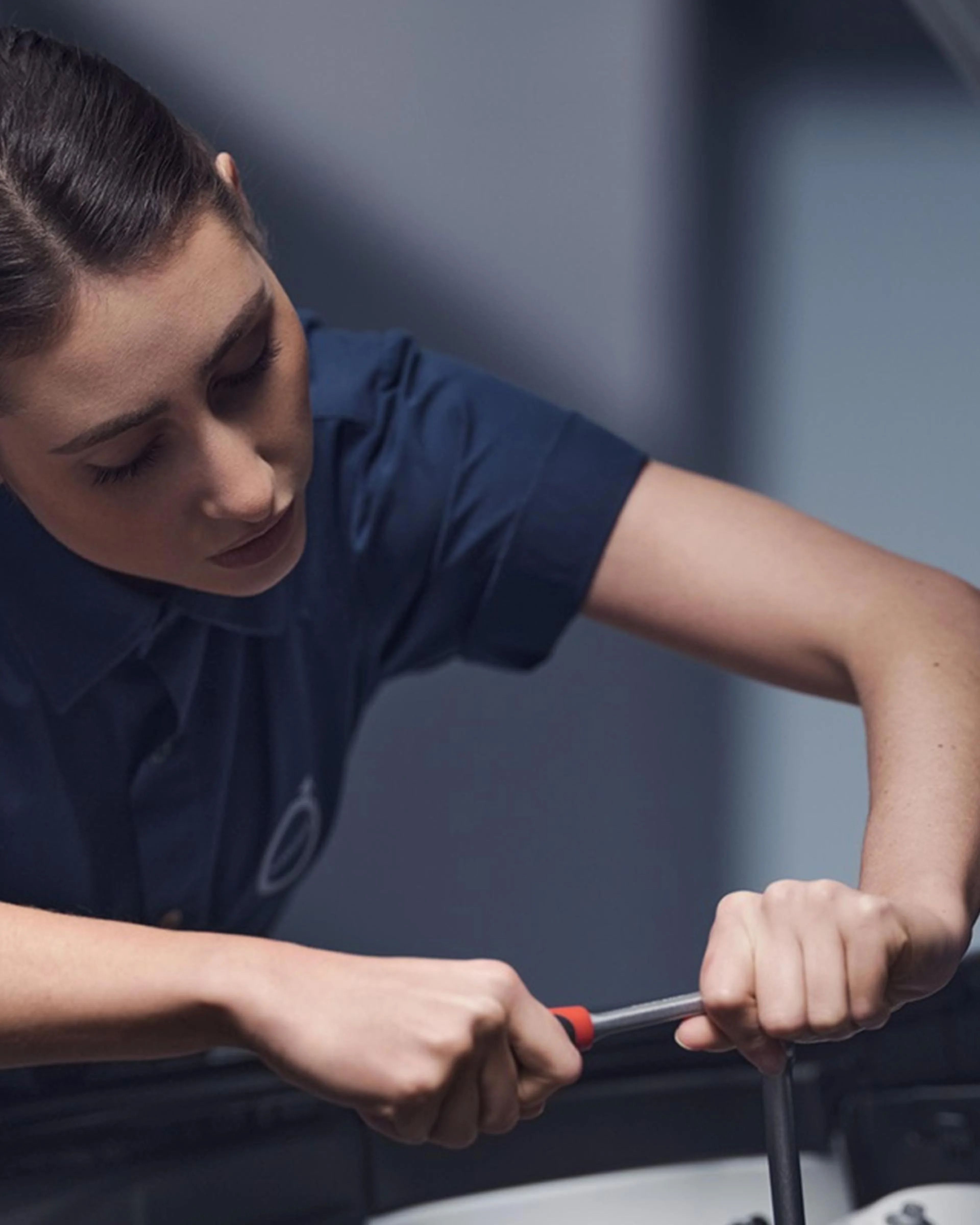 Eine Volvo Mechanikerin arbeitet mit einem Schraubenschlüssel bei geöffneter Motorhaube im Motorraum eines Volvo.