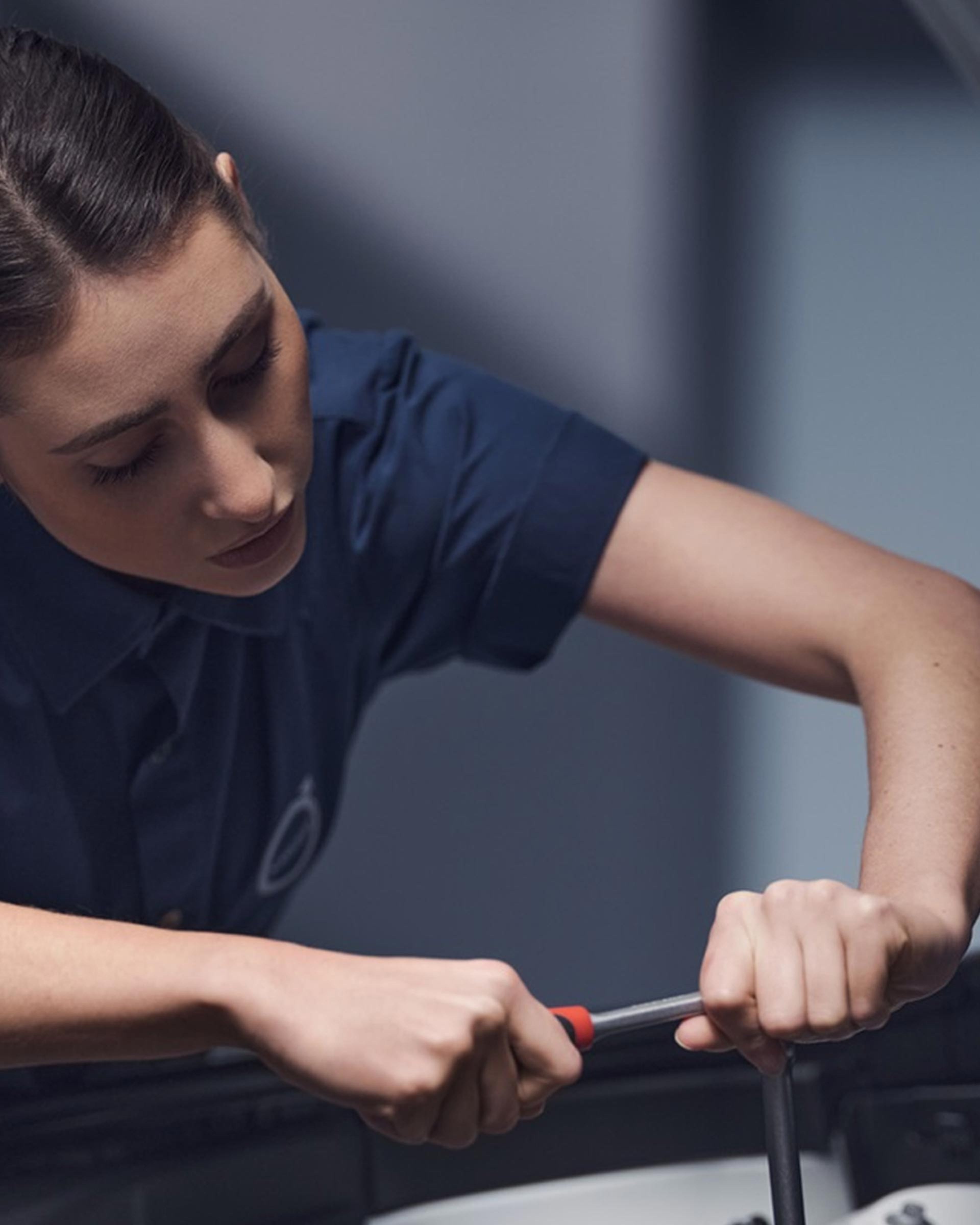 Eine Volvo Mechanikerin arbeitet mit einem Schraubenschlüssel bei geöffneter Motorhaube im Motorraum eines Volvo.