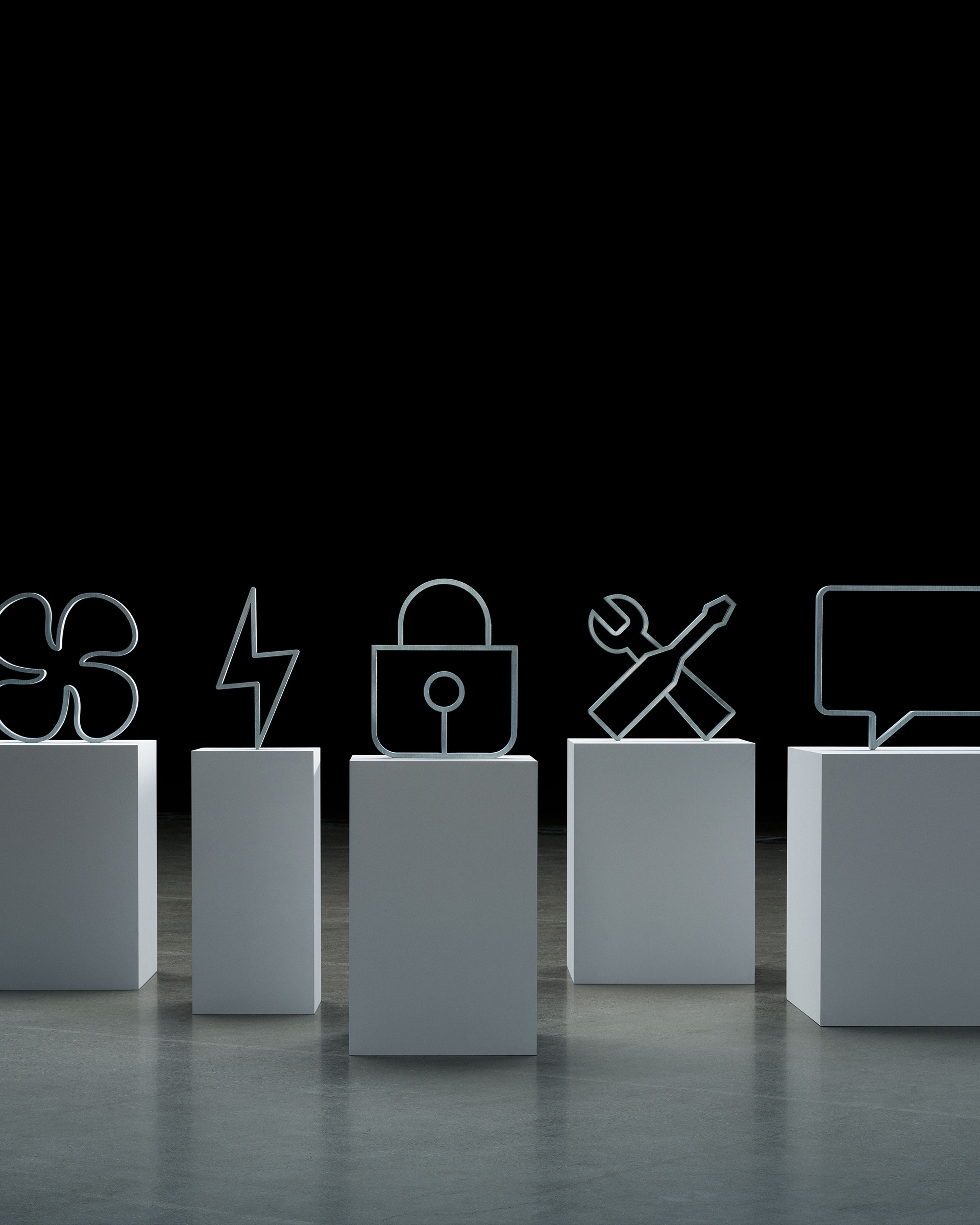 Viisi ikonin mutoista patsasta jalustalla: ropeli, salama, lukko, työkalut ristissä ja puhekupla..