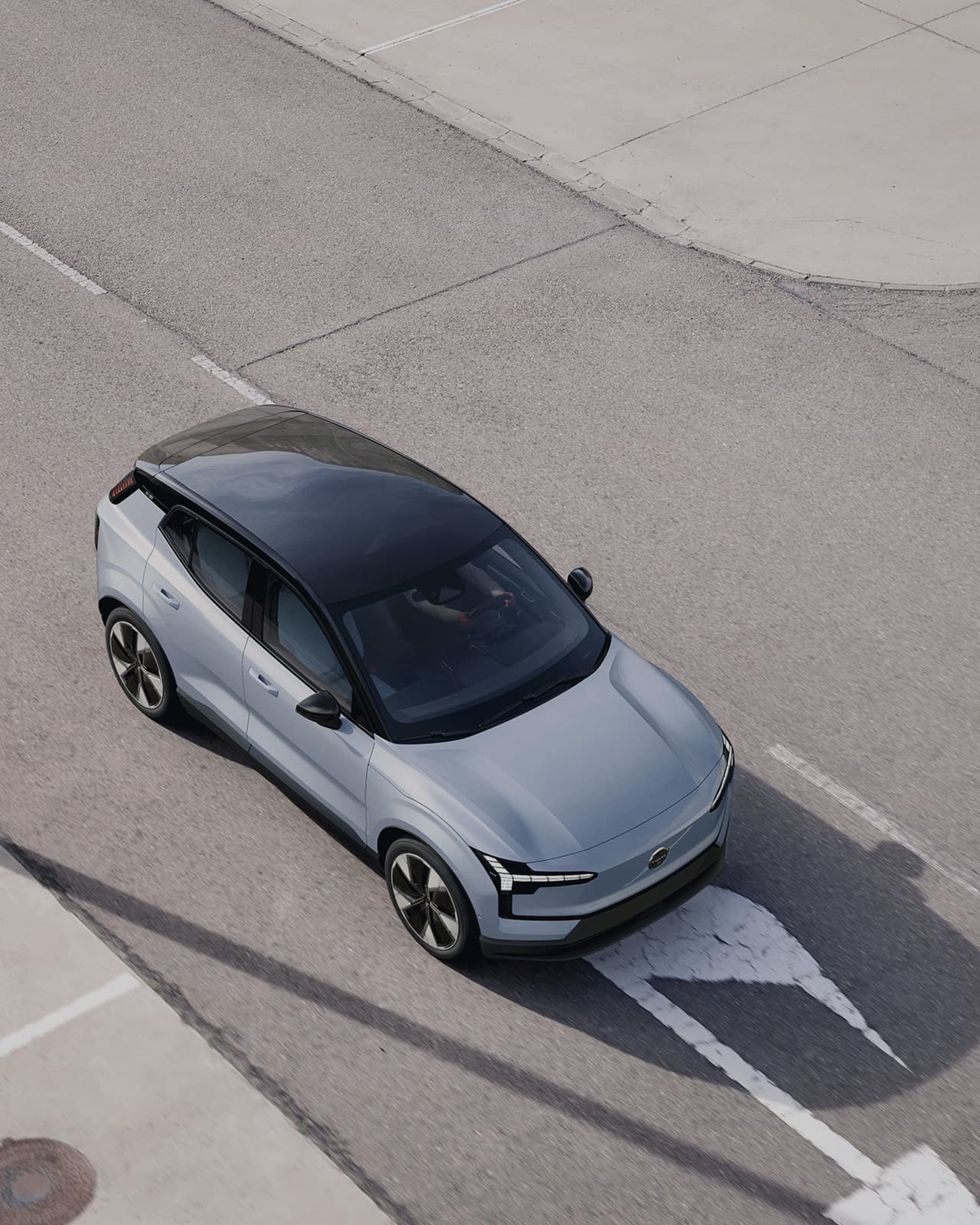 Zijaanzicht van een grijze Volvo EX30 met een zwart dak, geparkeerd op straat.