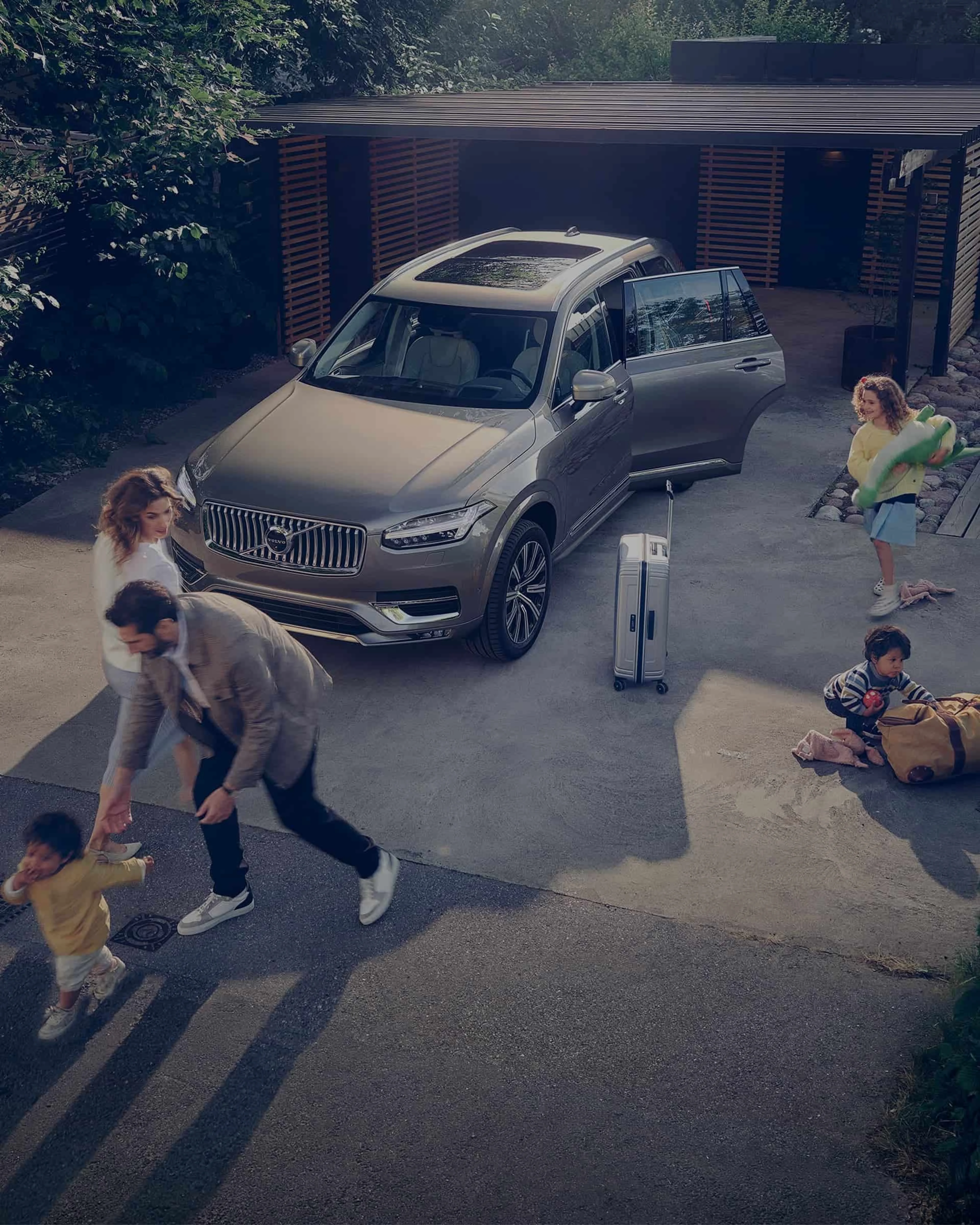 Une famille joue devant une Volvo XC60 avec la porte ouverte dans l'allée de leur maison.