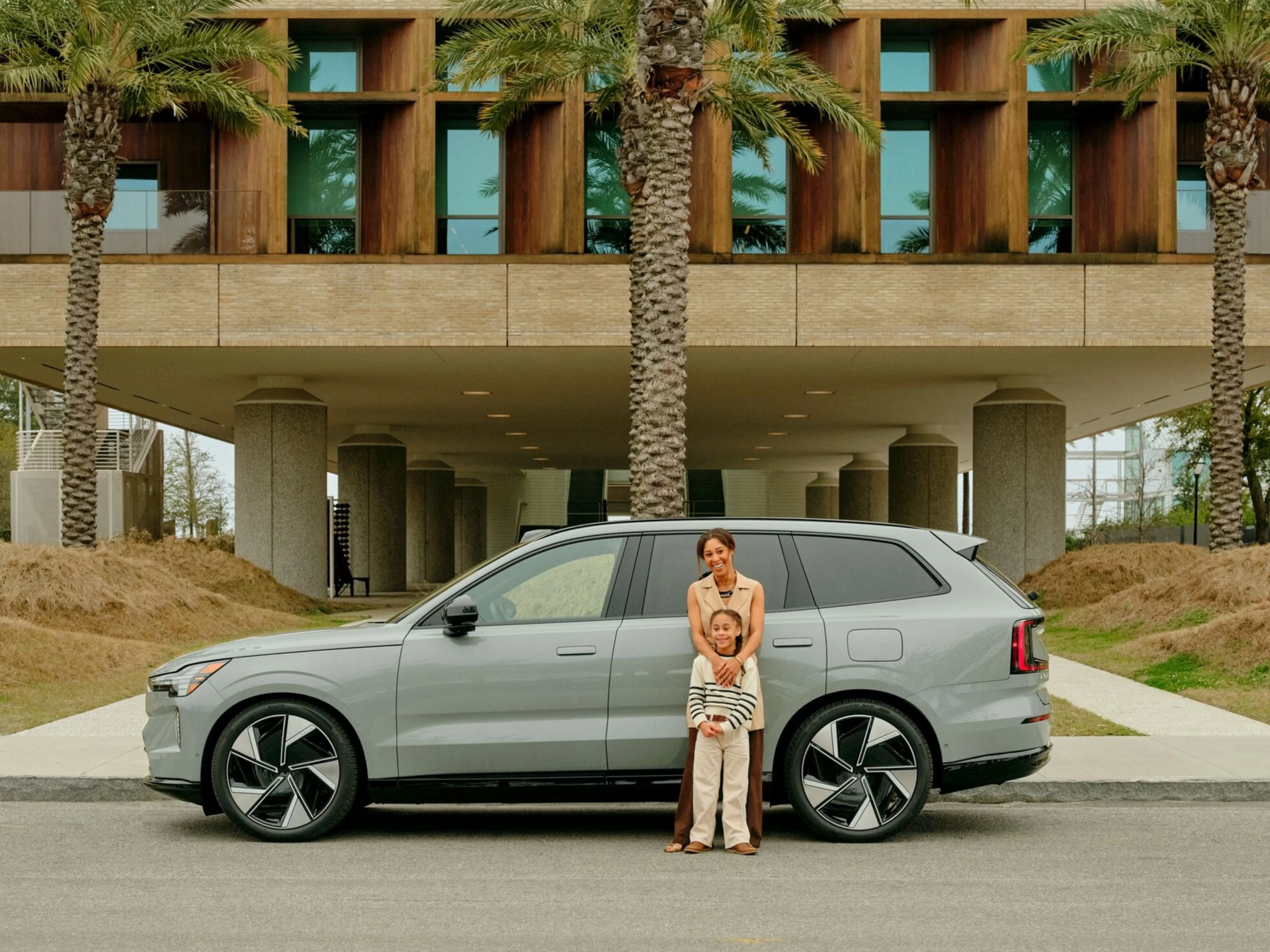 Volvo EX90 with family in front of building and palm trees