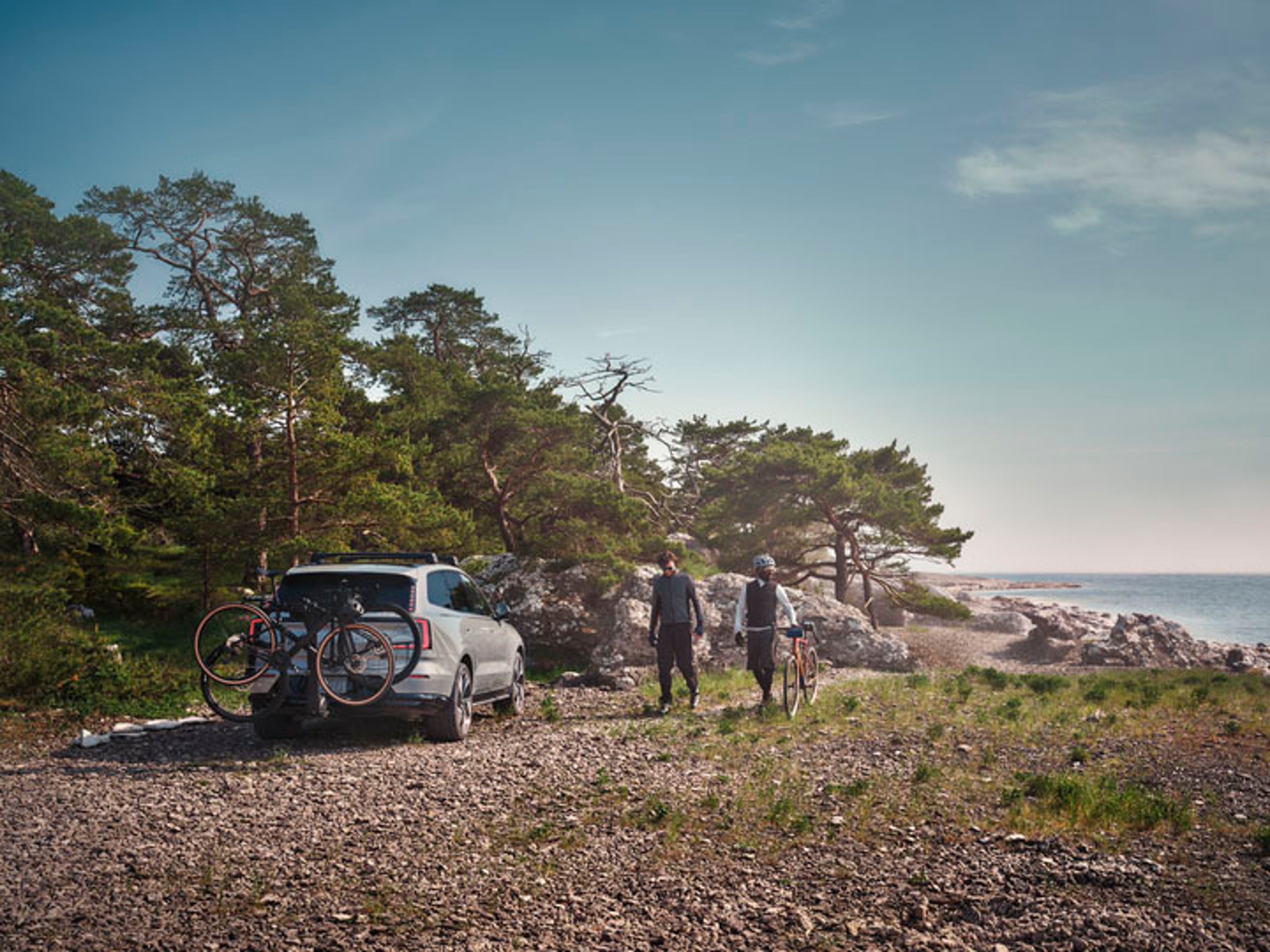 Dos ciclistas pasando junto a un EX90 eléctrico al lado del mar