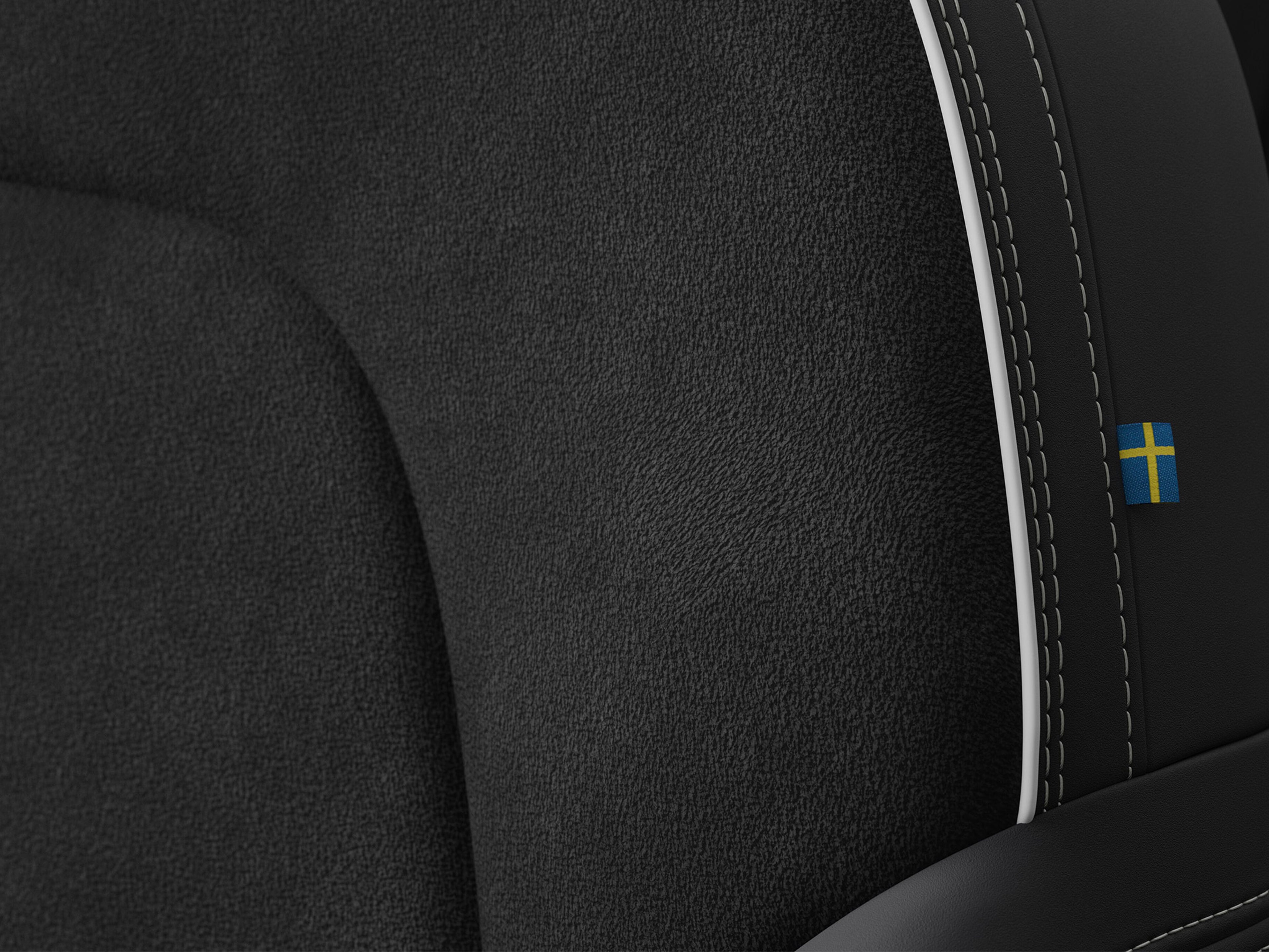 Yksityiskohta Volvo EX40 täyssähköauton penkistä, jossa on Charcoal -värinen kangas/microtech verhoilu "Connect". Saumassa pieni Ruotsin lippu.