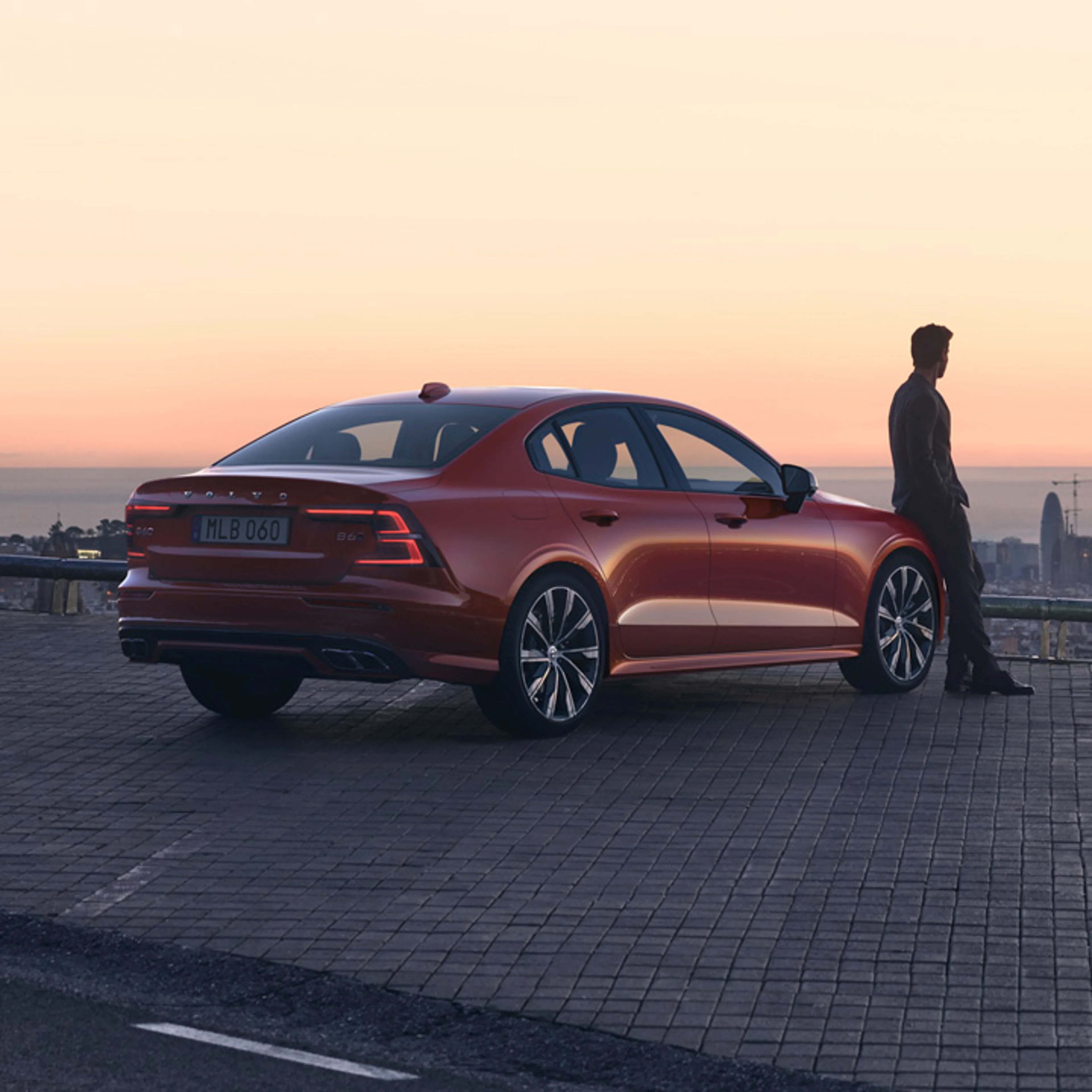 Un hombre mirando un amanecer recostado sobre un Volvo S60 color rojo