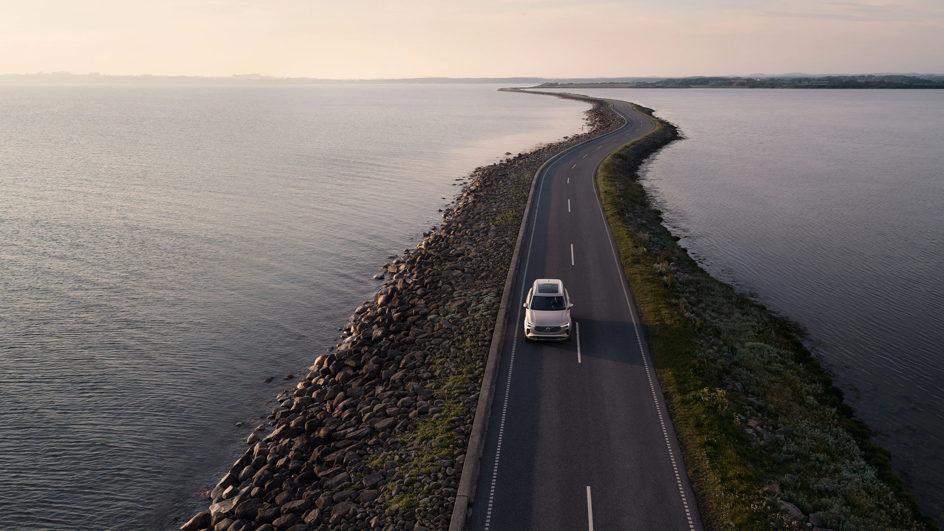Ein Volvo in Bright Dusk fährt über eine schmale Landstraße auf dem Meer.