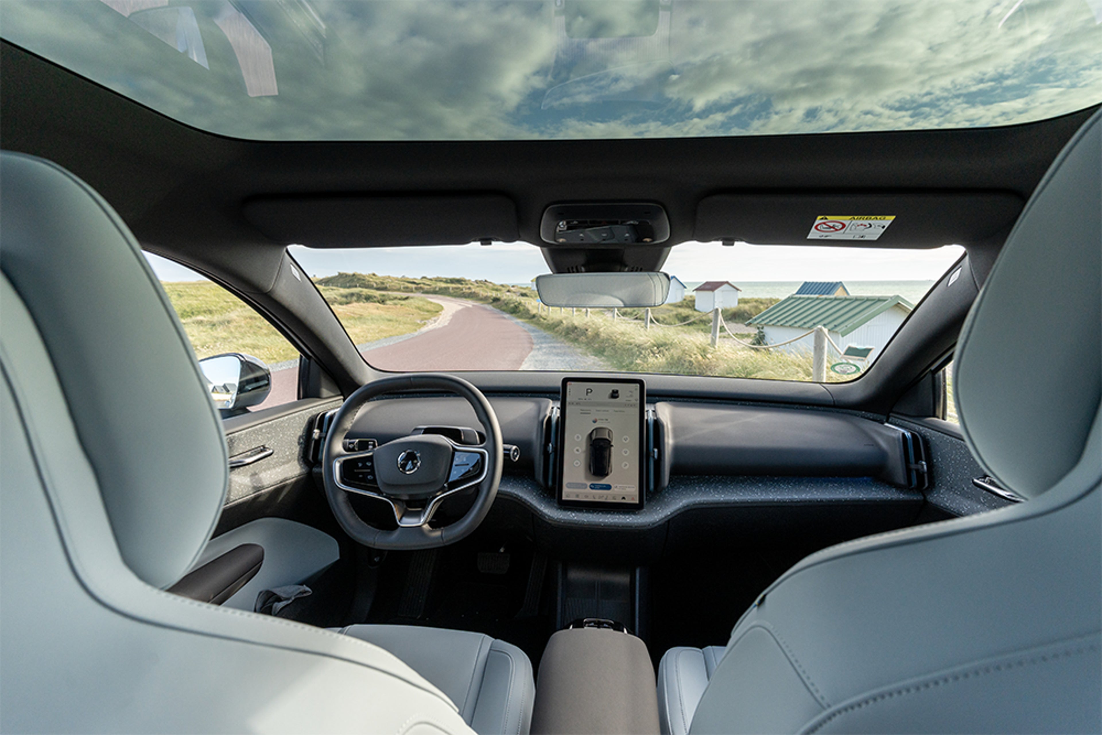 Intérieur d'une Volvo électrique avec grand écran tactile, volant moderne et toit panoramique, route visible.