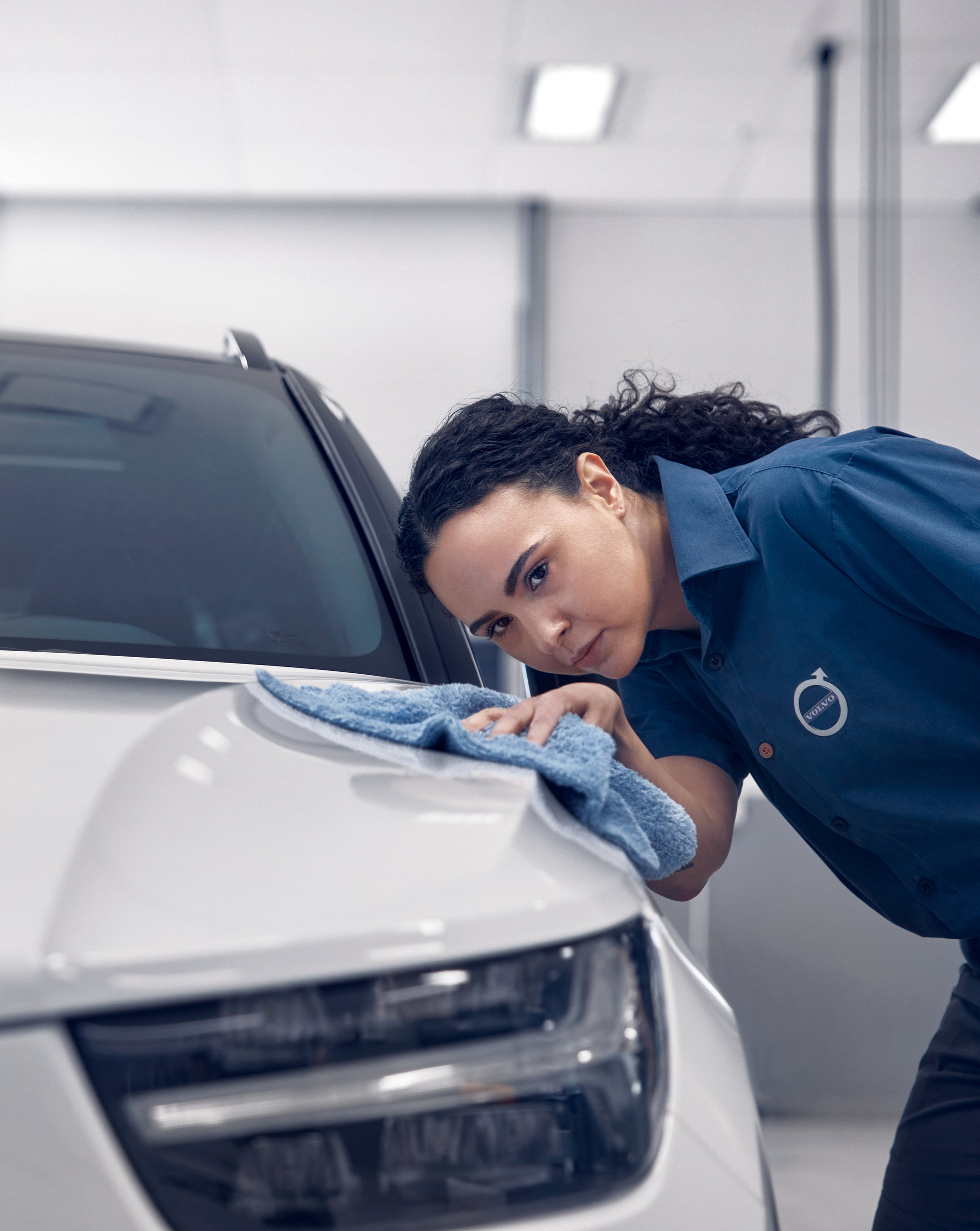 Technicien polissant l'avant d'une voiture blanche avec un chiffon bleu, en intérieur