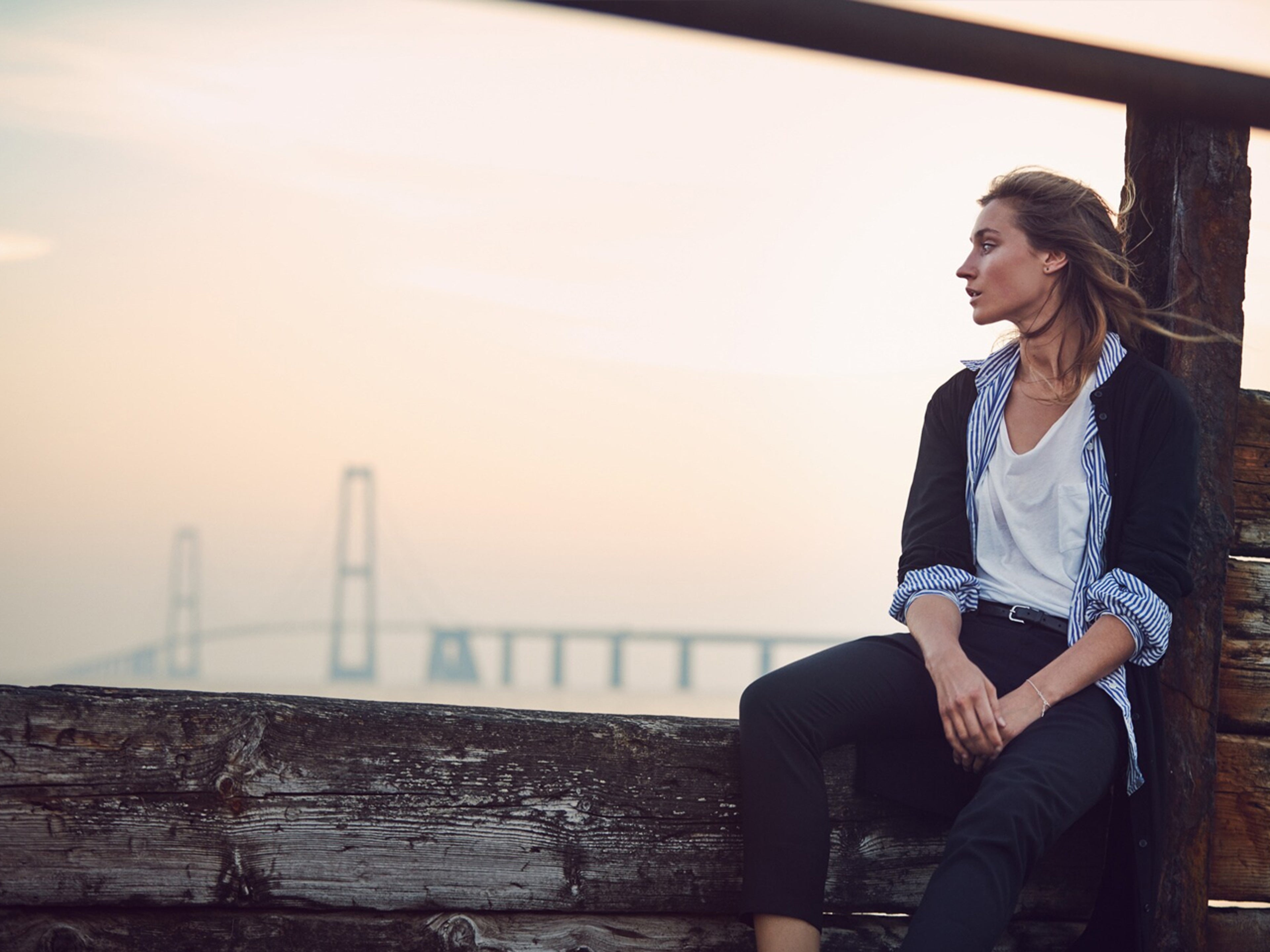 Dame som sitter ved en kai i solnedgang