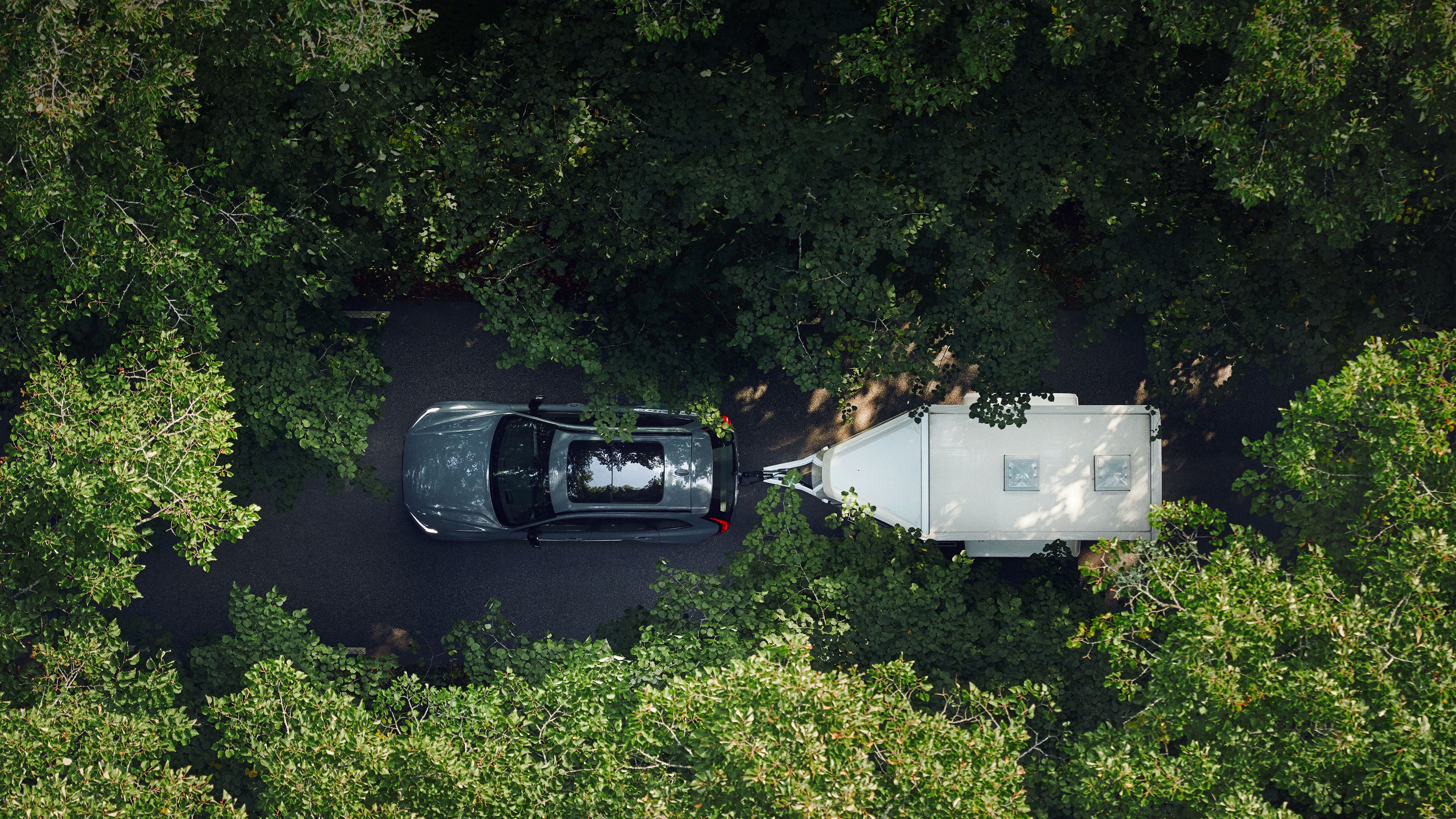 An overhead image of the Volvo XC60 Plug-in hybrid towing a trailer through a forest.