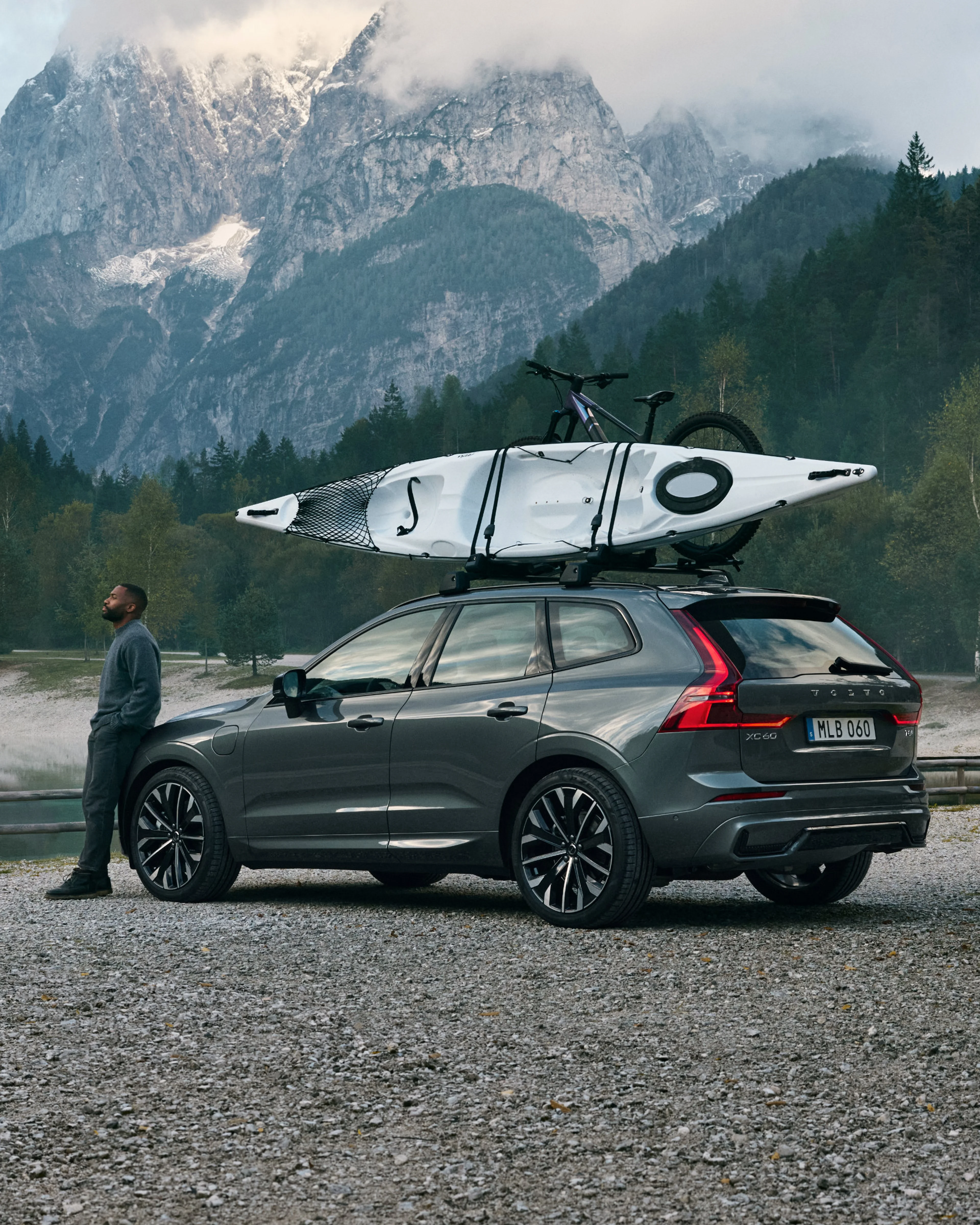 Der Volvo XC60 in der Farbe Forest Lake (dunkelgrün) steht im Wald vor einem See.