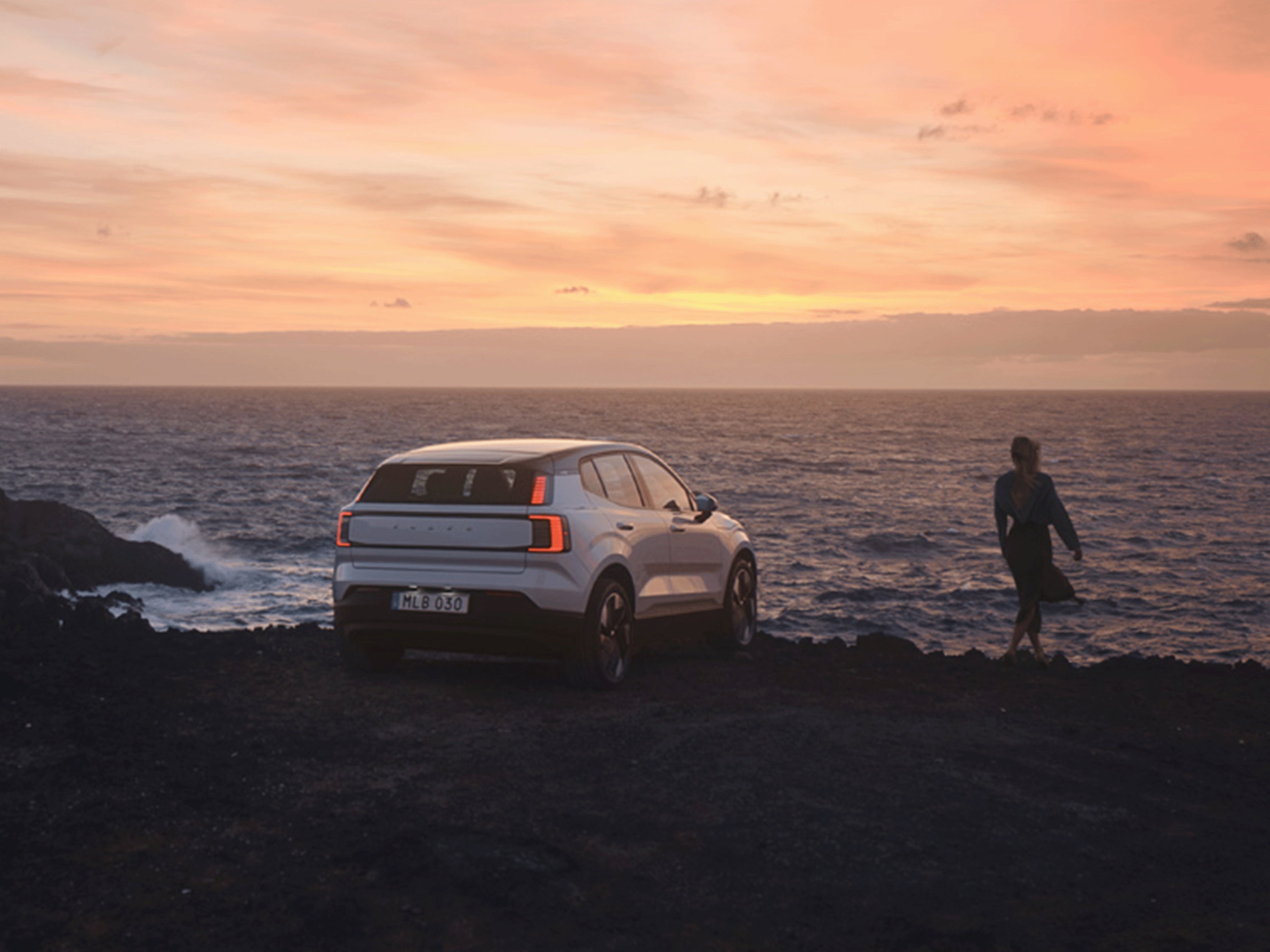 Eine Person steht neben einem Volvo an einer Küste.