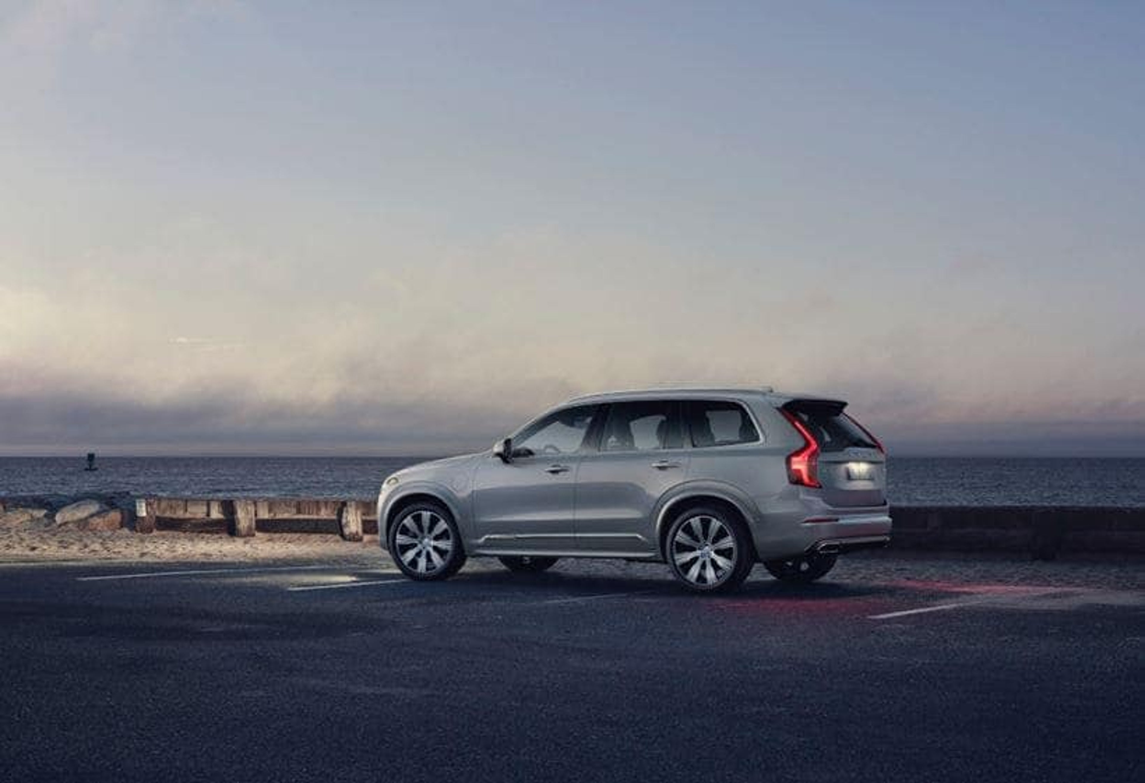 Ein silberner Volvo XC90 SUV steht am Meer und es ist Abend.