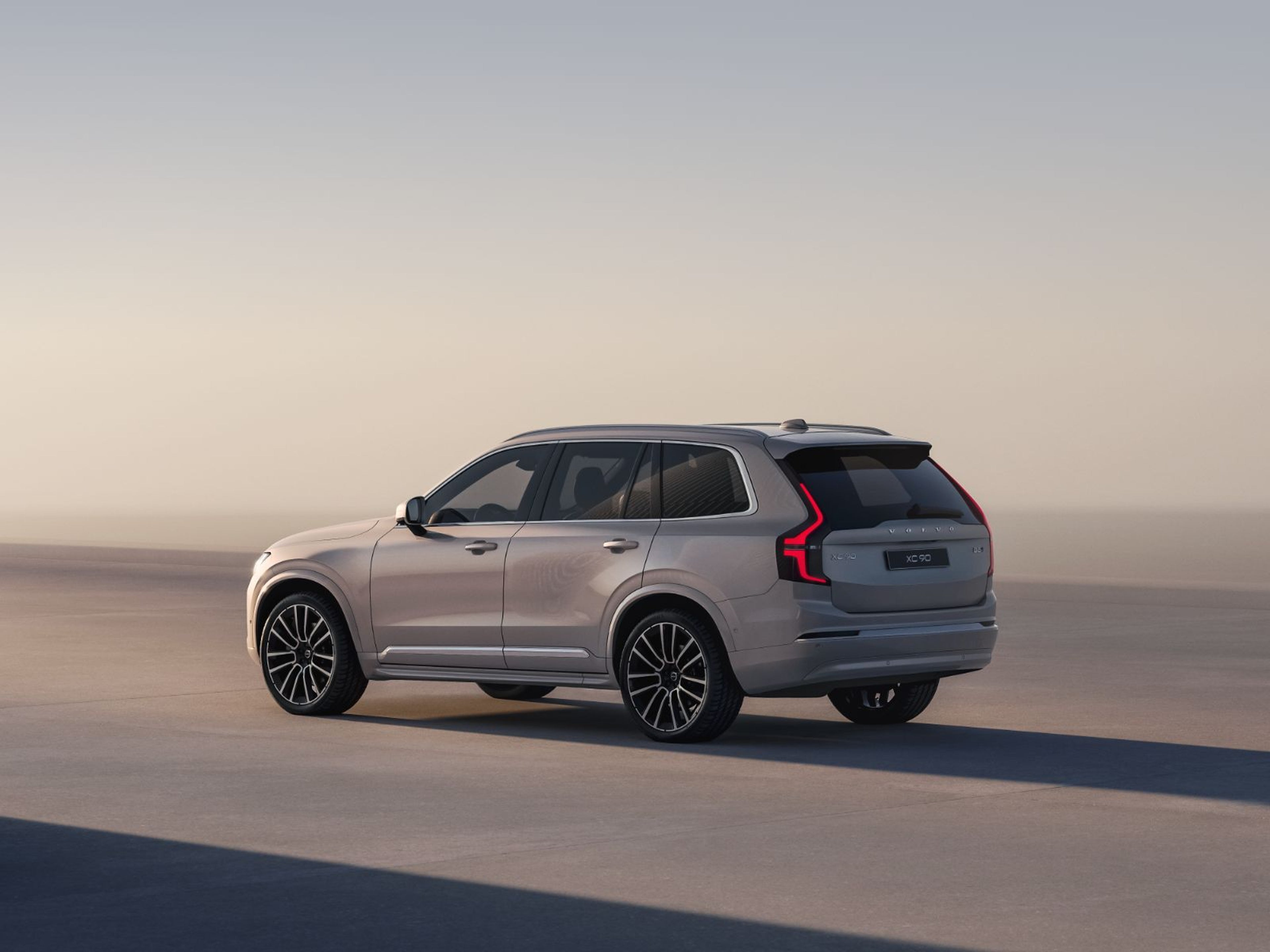Luksuzni Volvo XC90 SUV u boji Bright Dusk, parkiran na širokoj betonskoj površini pod nježnim svjetlom sumraka, ističući prepoznatljiva stražnja svjetla i elegantne linije.