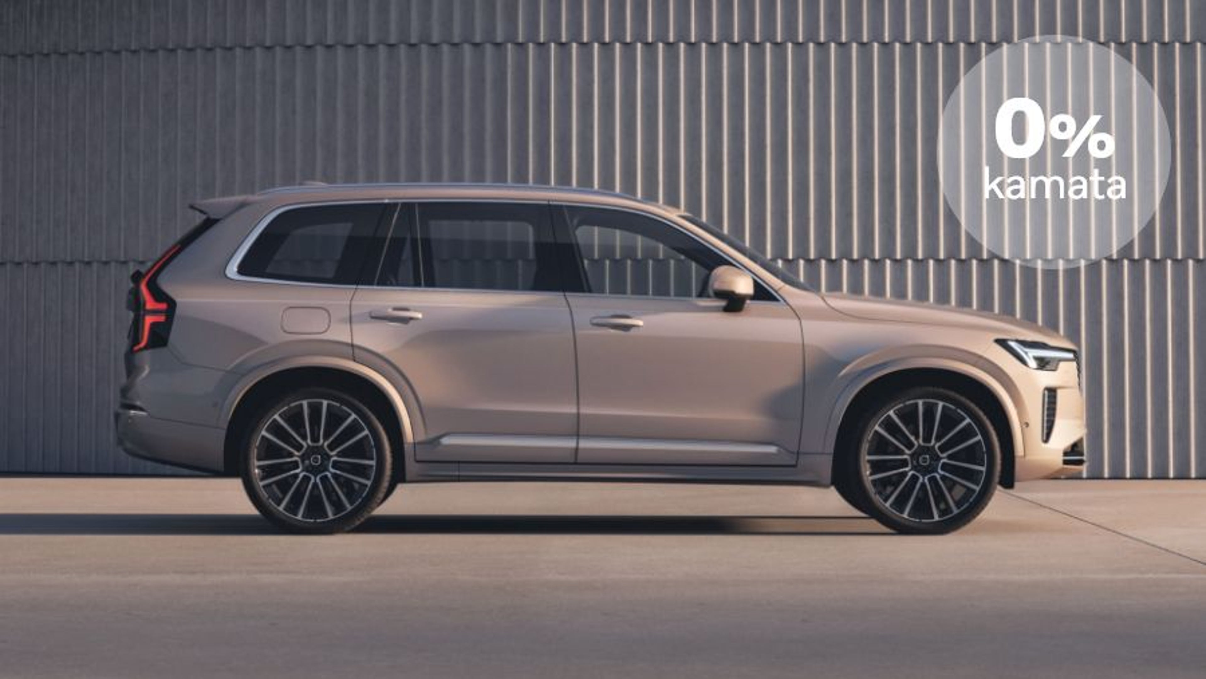 Srebrni Volvo XC60 SUV parkiran ispred kamenog zida, s plavim krugom u gornjem desnom kutu na kojem piše "0% kamata"