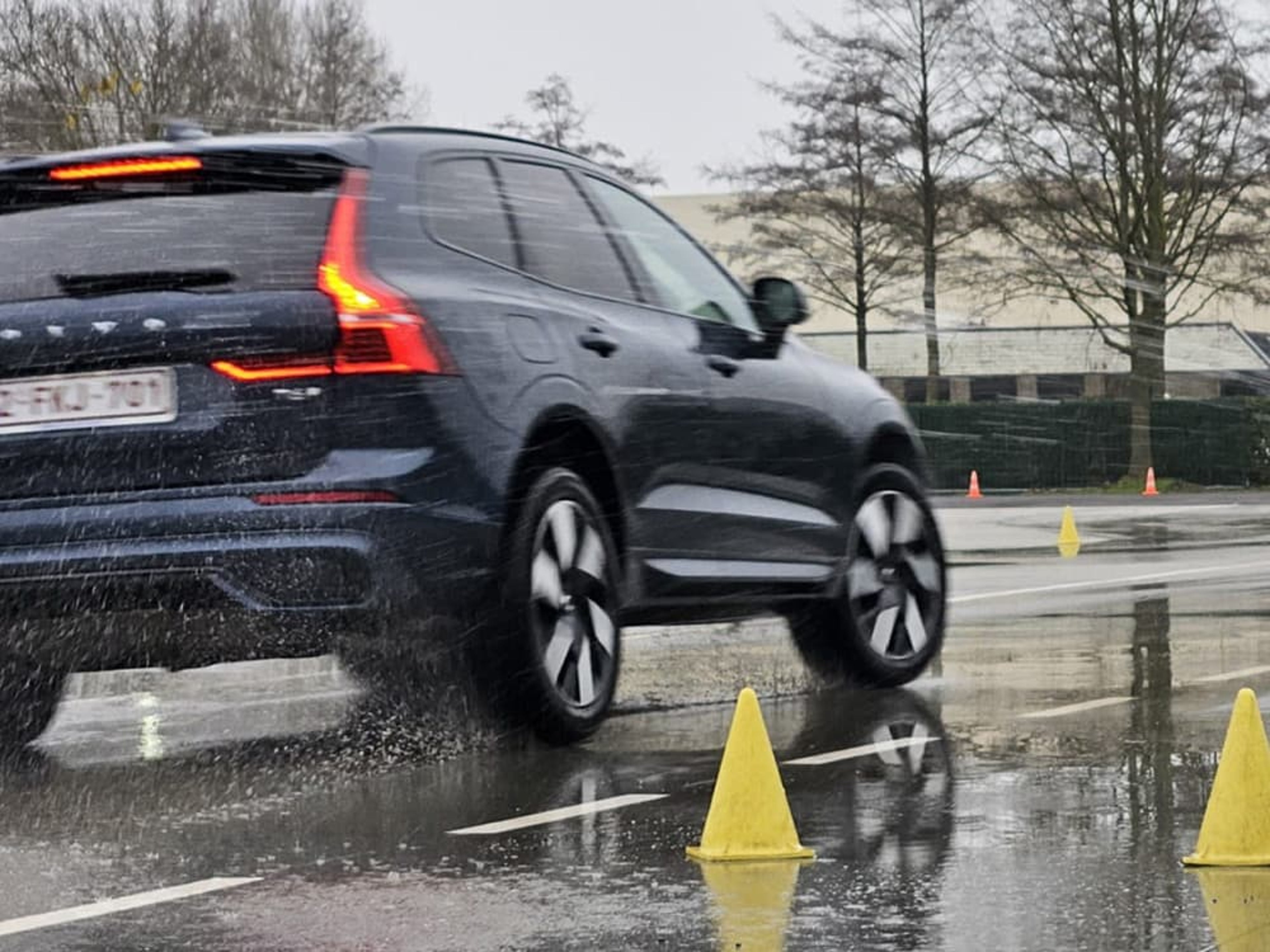 Een donkere Volvo EX30 rijdt door een plas water, waardoor er veel opspattend water ontstaat.