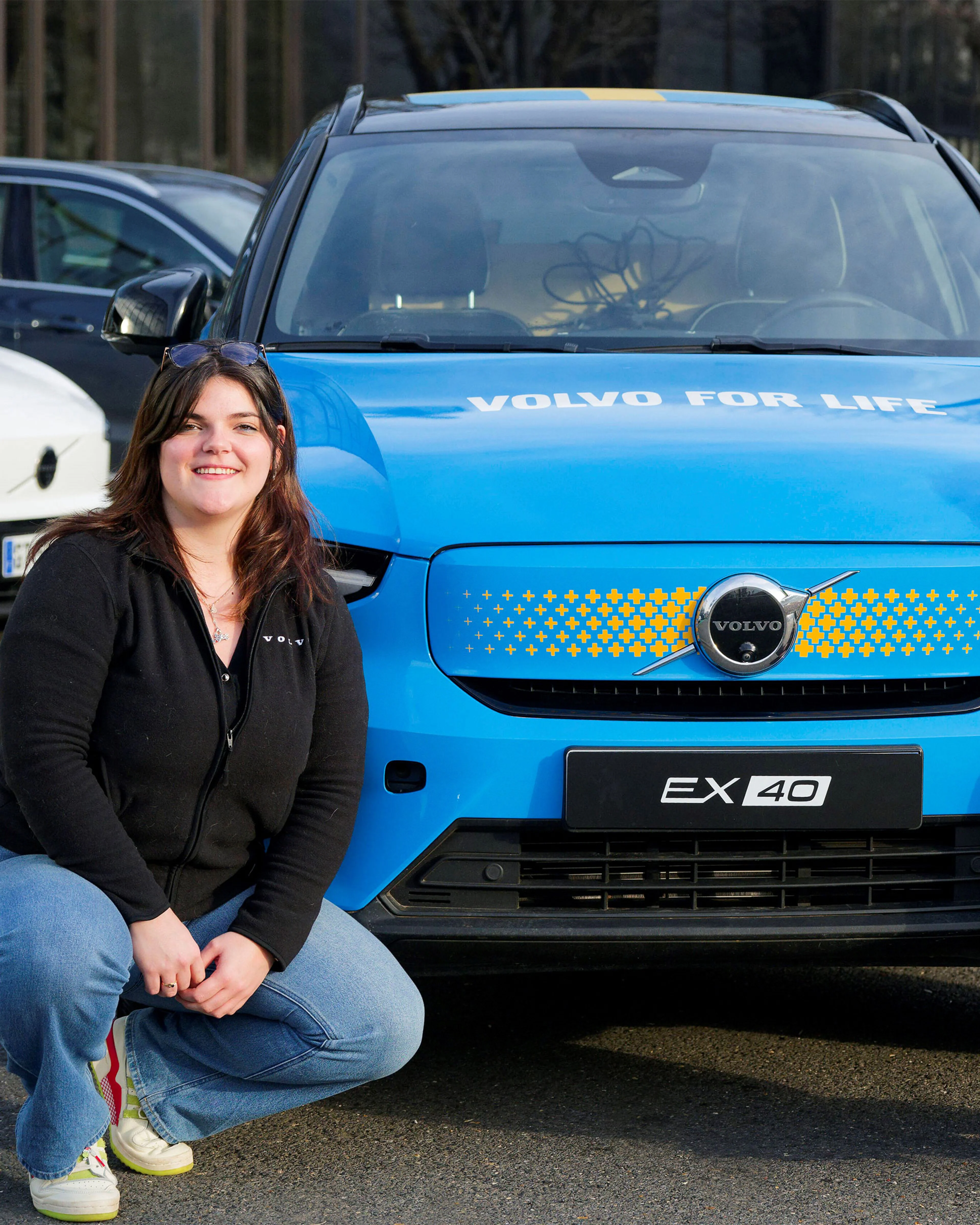 Marie Brabant et Séverine Mary agenouillées devant une Volvo EX40 bleue avec "VOLVO FOR LIFE" écrit sur le capot