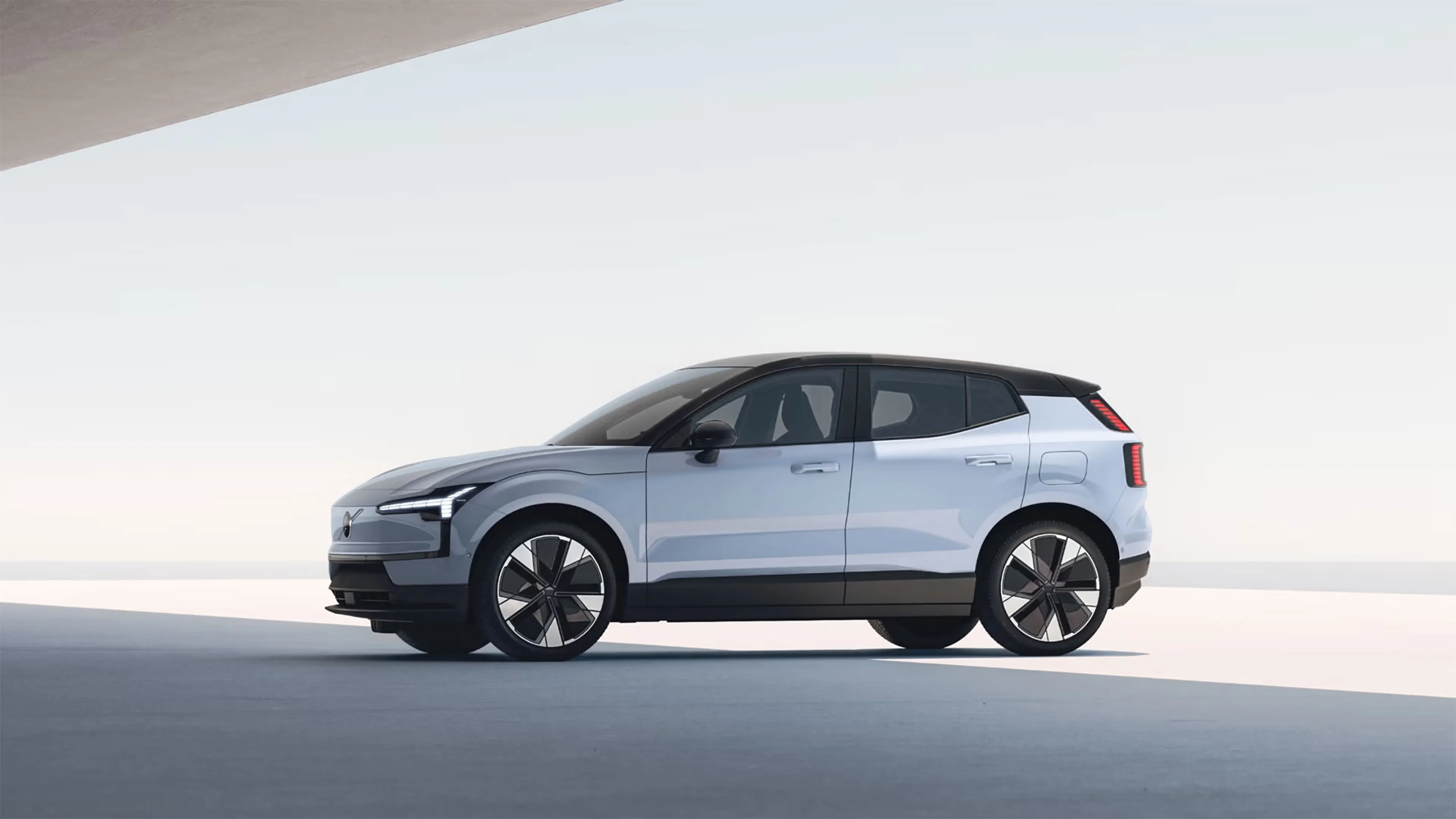 Vue latérale d’une Volvo EX30 blanche moderne avec toit noir et grandes roues, dans un décor minimaliste