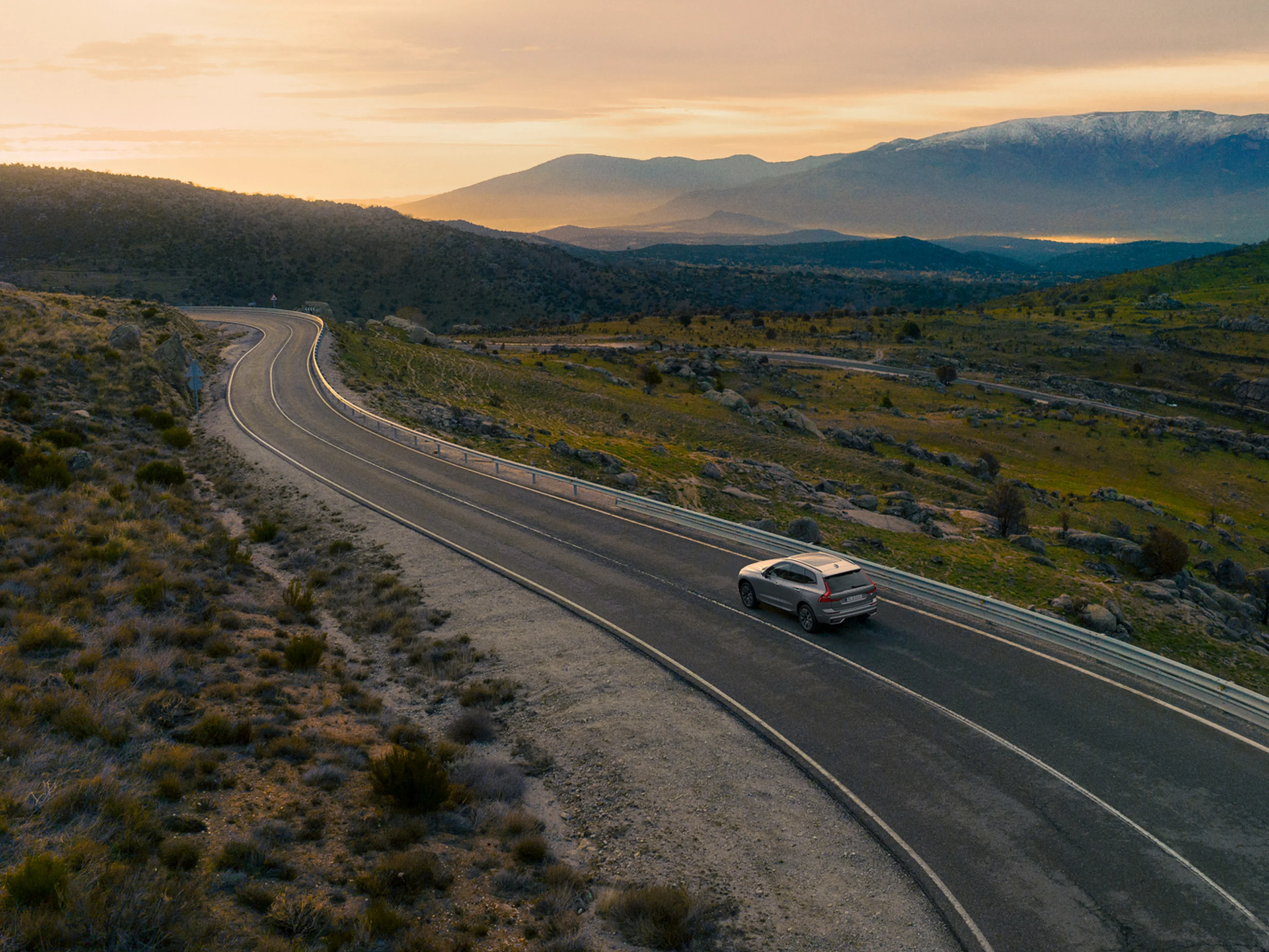 Silver Dawn -värinen Volvo XC60 ajaa vuoristotiellä auringonlaskun aikaan.