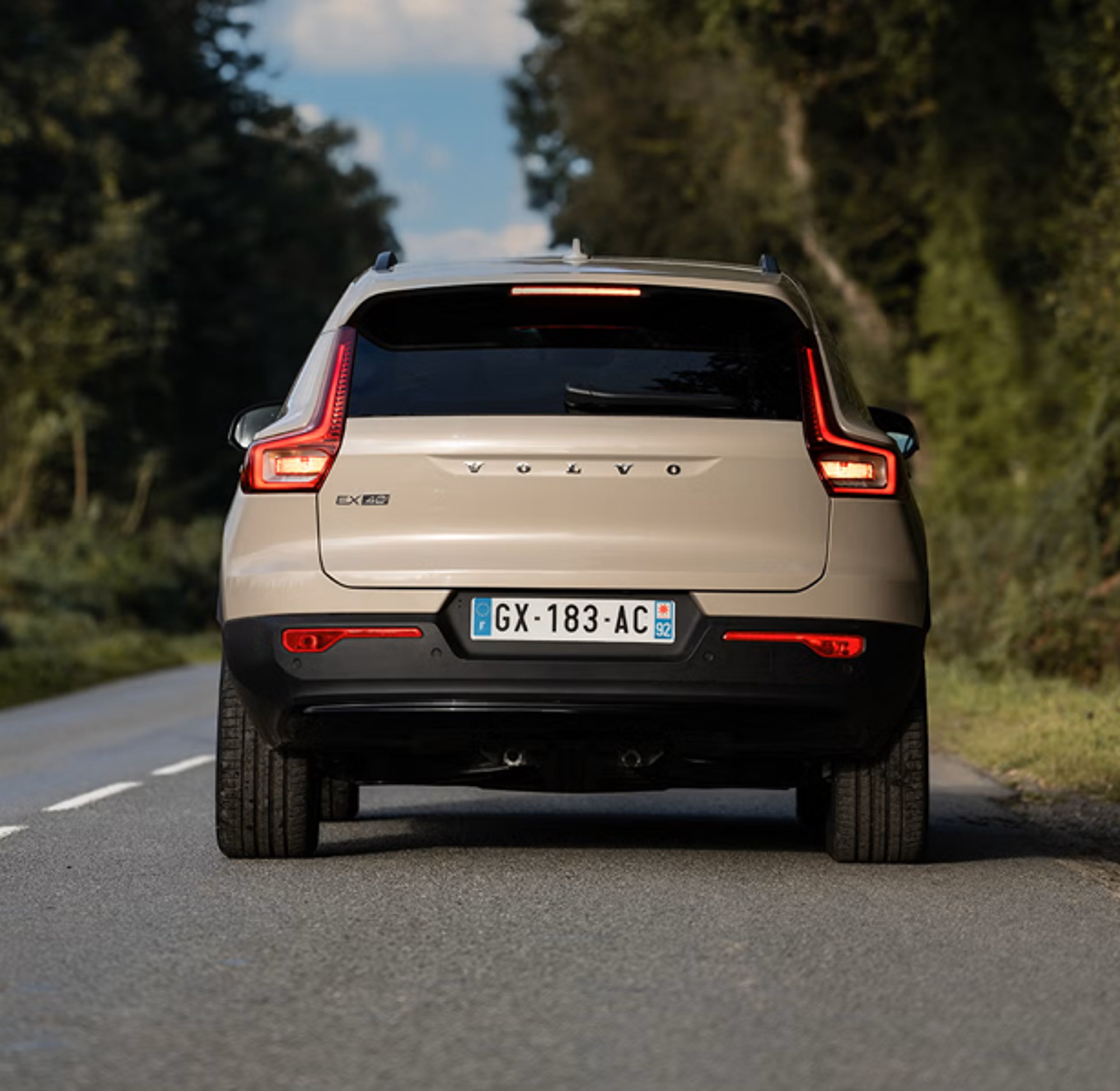 Vue arrière d’un SUV Volvo beige sur route bordée d’arbres, plaque GX-183-AC visible.