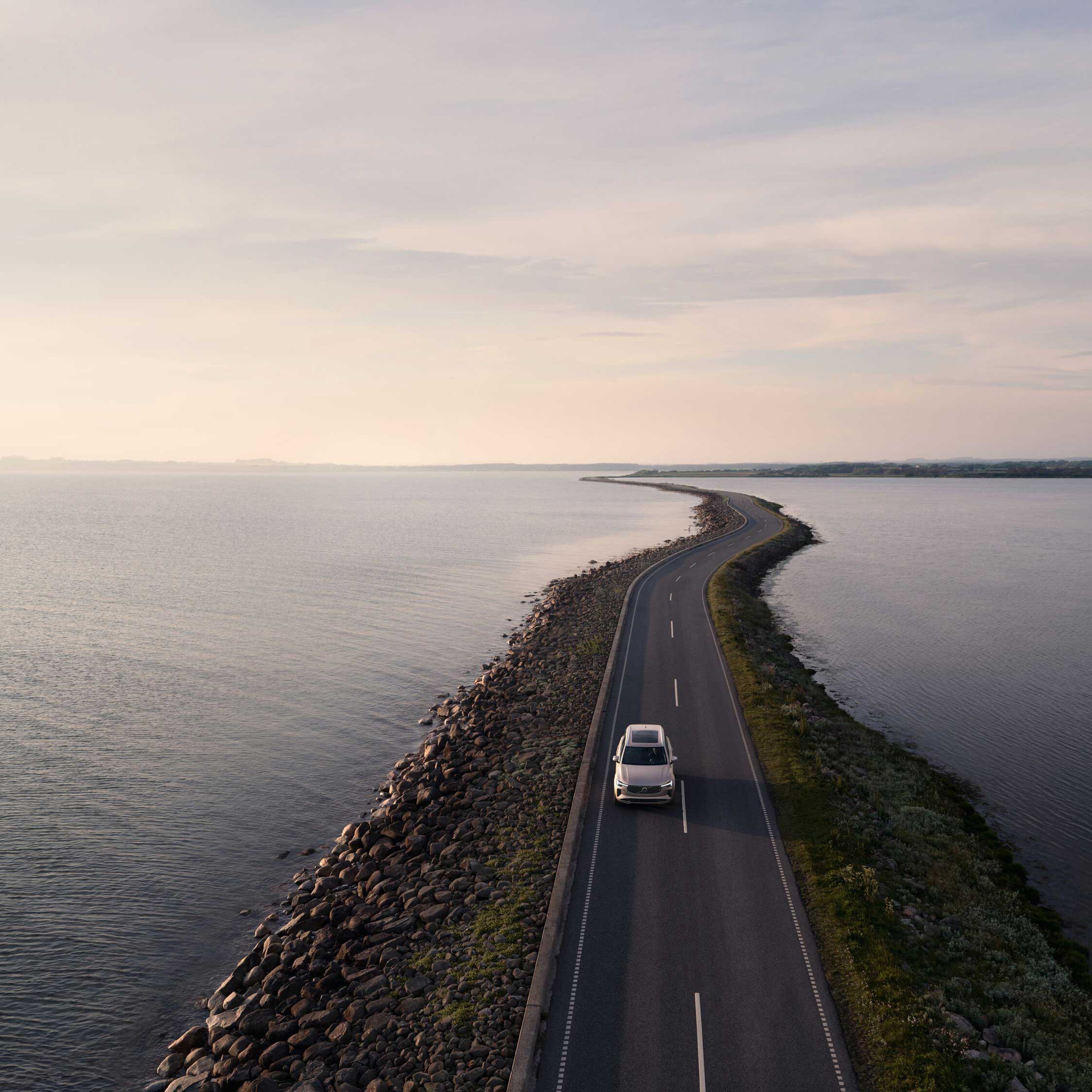 En stor bil fra Volvo kører på en vej med vand på hver side, set oppefra i fugleperspektiv.