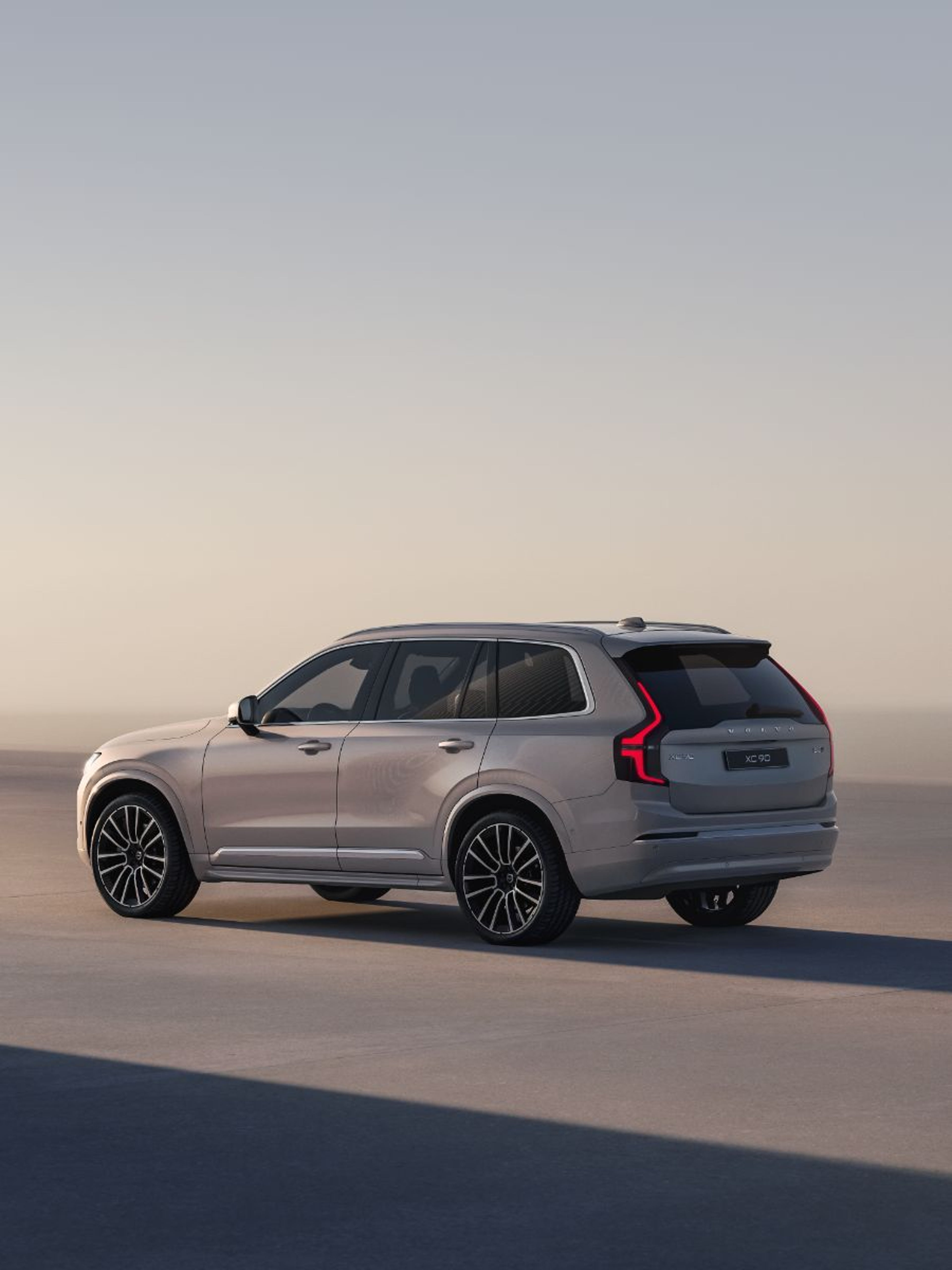 Srebrni Volvo XC90 prikazan iz zadnjega bočnega kota, parkiran v studijskem okolju ob mehki svetlobi ob sončnem zahodu.