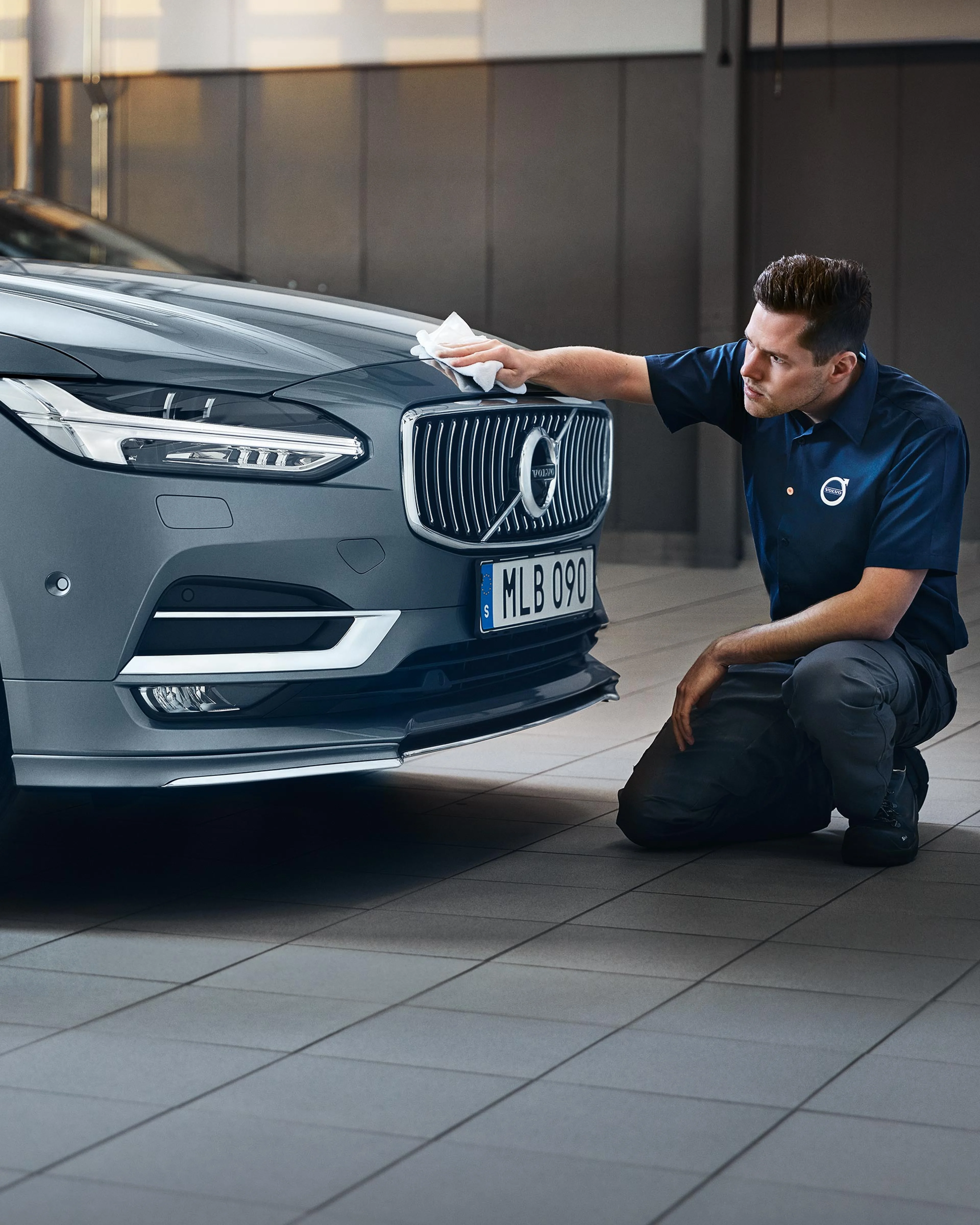 Ein Volvo Service Techniker wischt hockend mit einem Fließtuch über die Kühlerhaube eines Volvo S90.