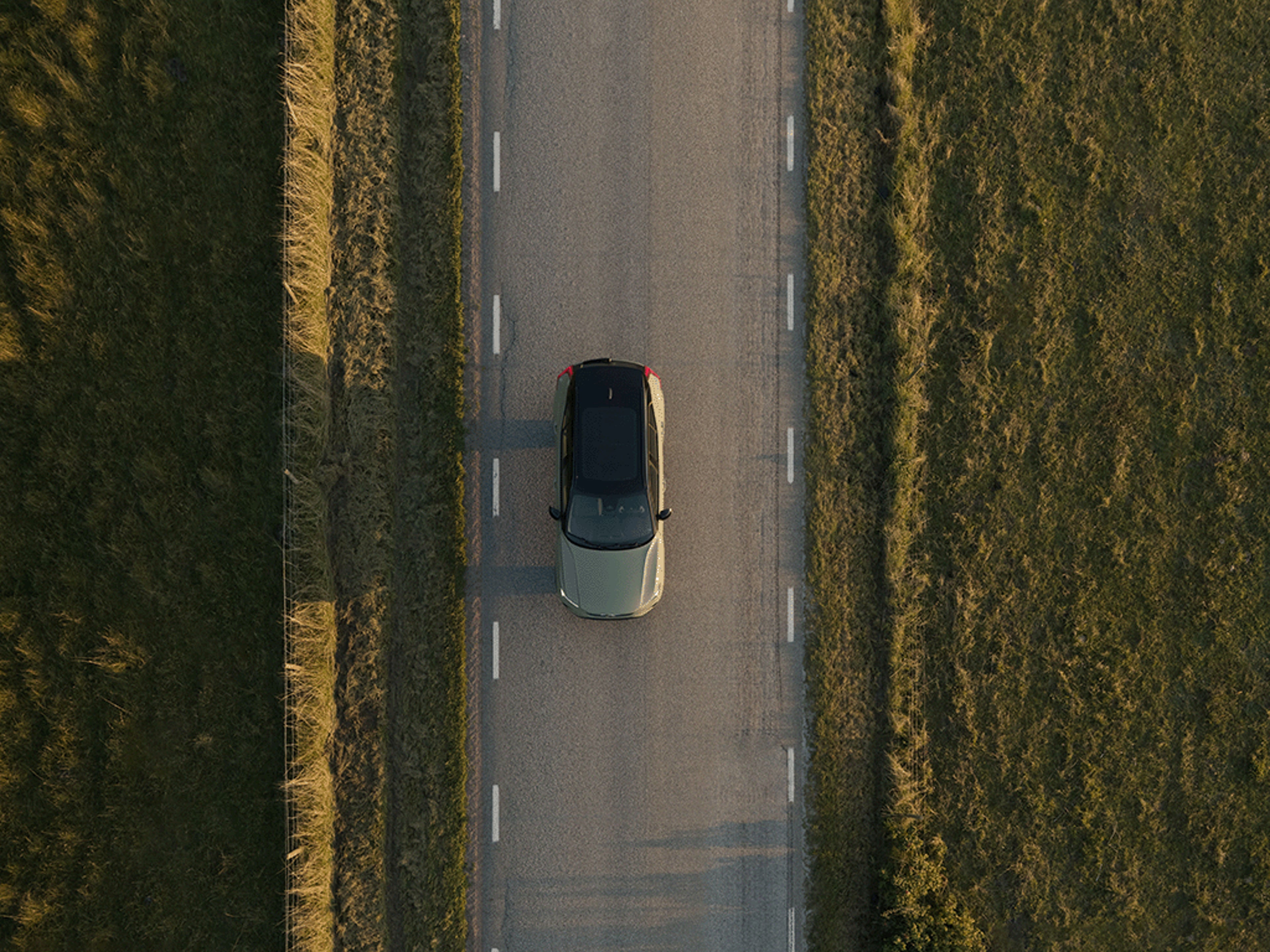 Vogelperspektive von einem Volvo XC40 Recharge auf einer Straße zwischen Feldern.