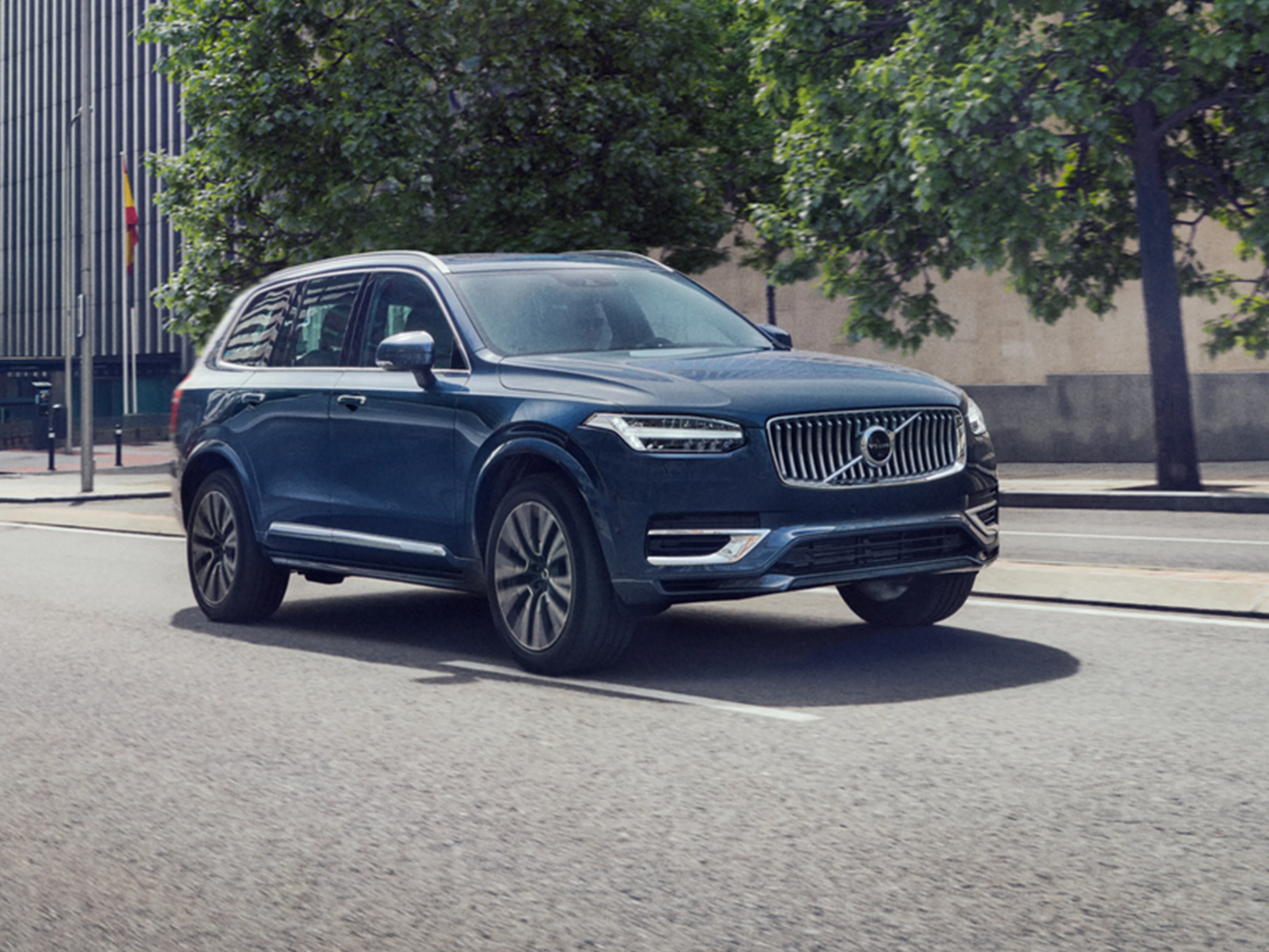 Denim Blue -värinen Volvo XC90 lataushybridiauto ajaa bulevardikadulla auringonpaisteessa..