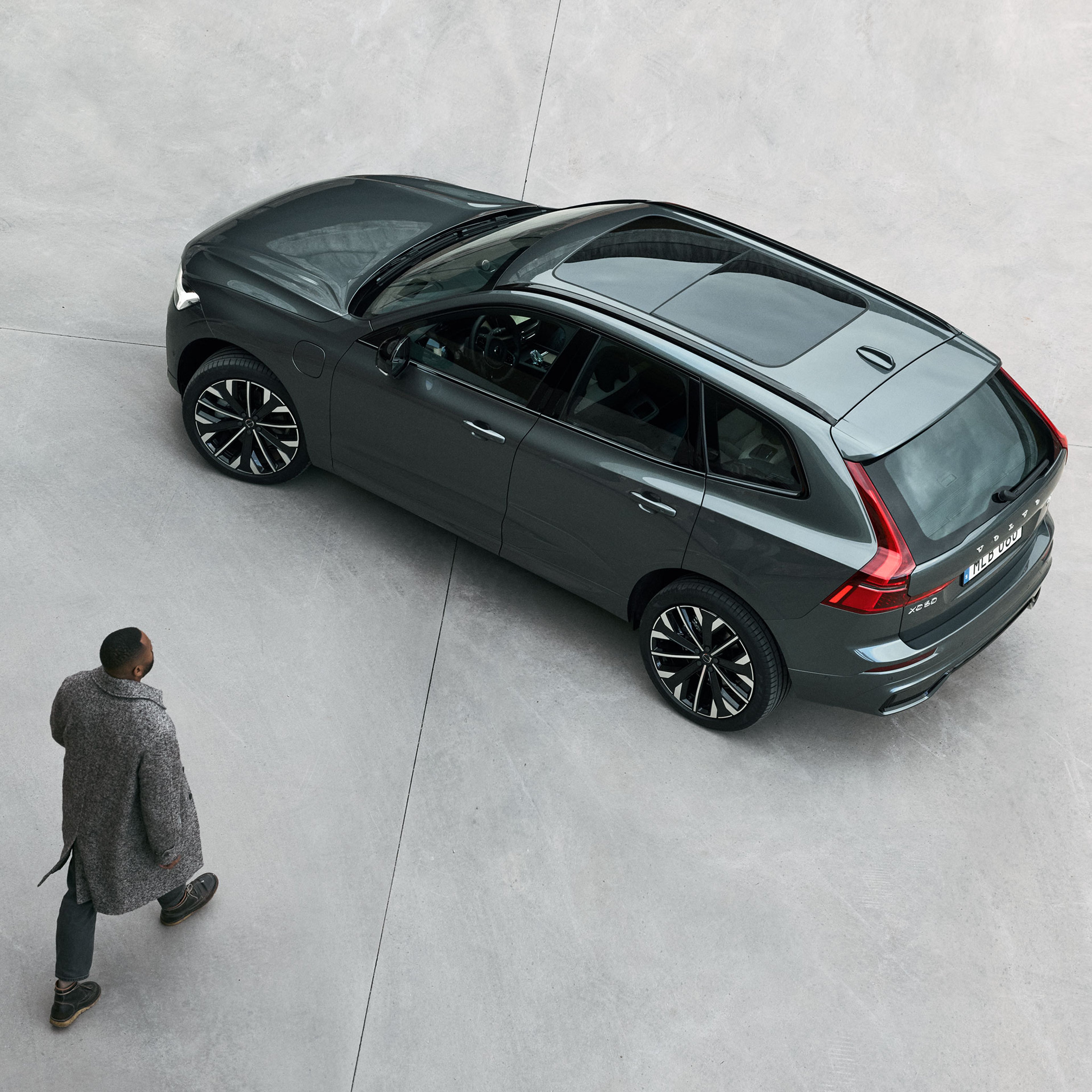 Mies kävelee kohti kivialustalle pysäköityä Forest lake -väritstä Volvo XC60 lataushybridikatumaasturia.