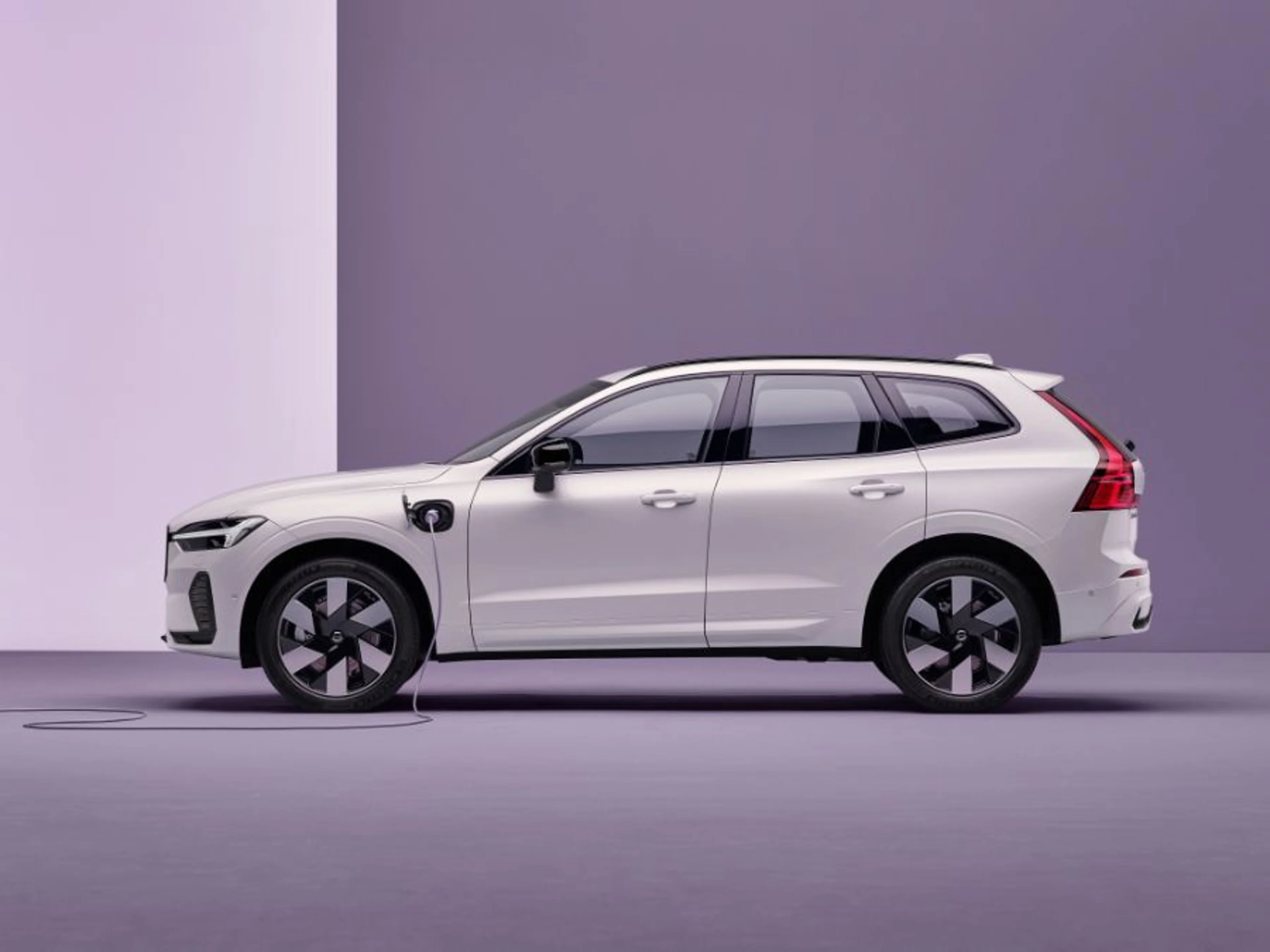 Volvo XC60 Plug-in Hybrid SUV u svijetlo sivoj boji, priključen na punjenje s vidljivim kablom, parkiran u prostranom krajoliku pod blagim svjetlom, simbolizirajući jednostavnost punjenja i ekološku mobilnost.