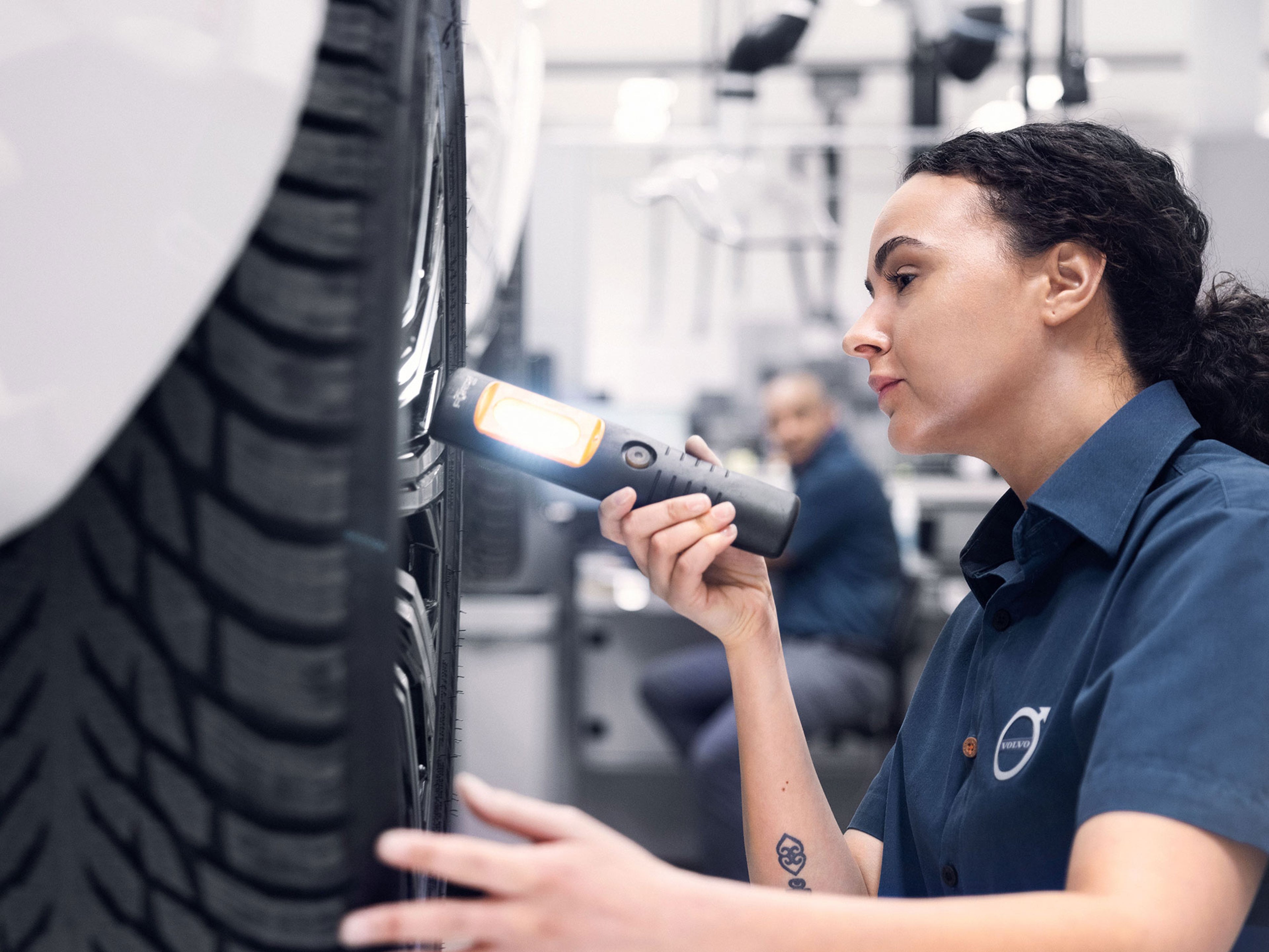 Une mécanicienne en uniforme Volvo inspecte un pneu de voiture avec une lampe de poche.