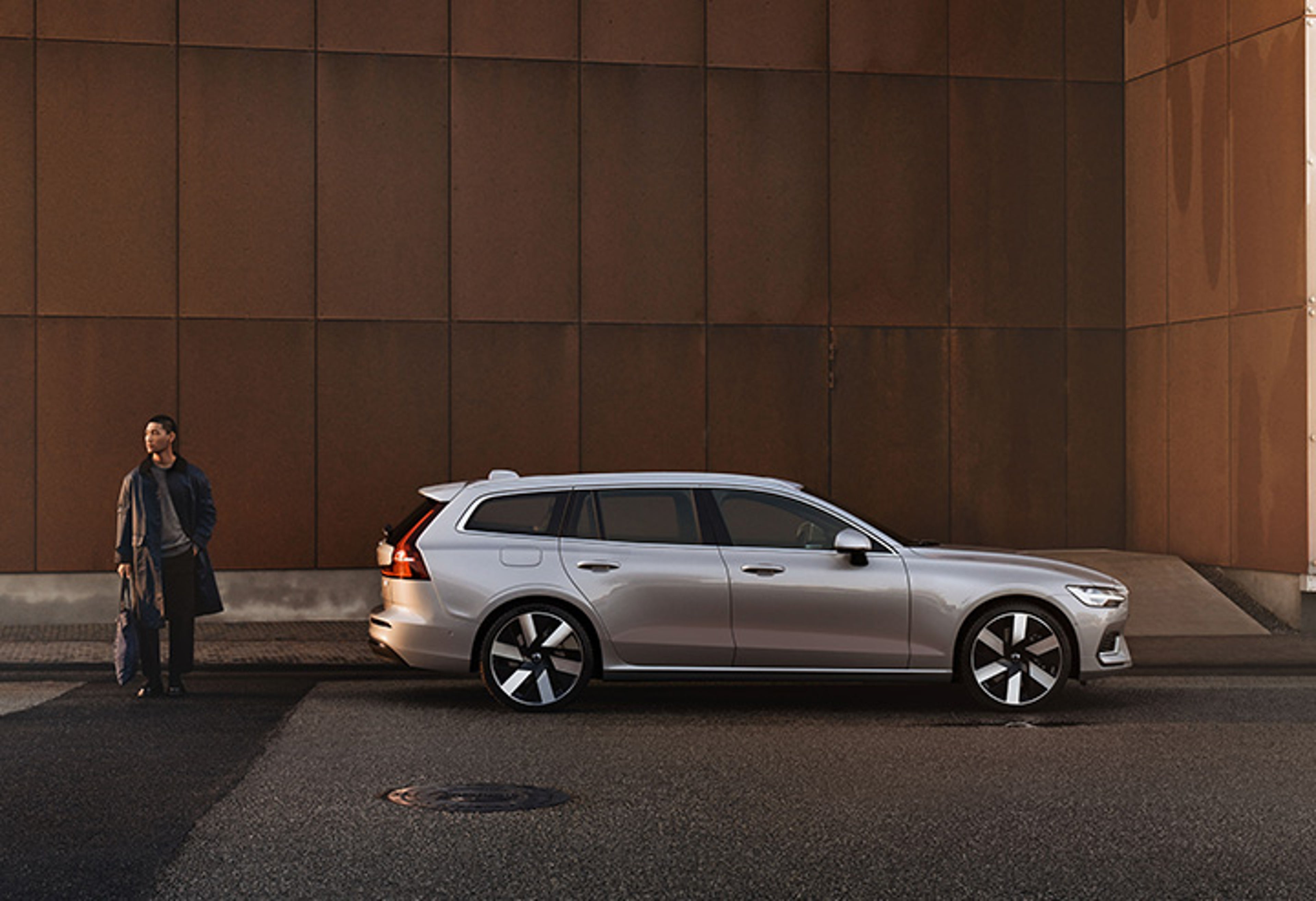 Eine Person mit Tasche steht hinter einem silbernen Volvo V60 Kombi.