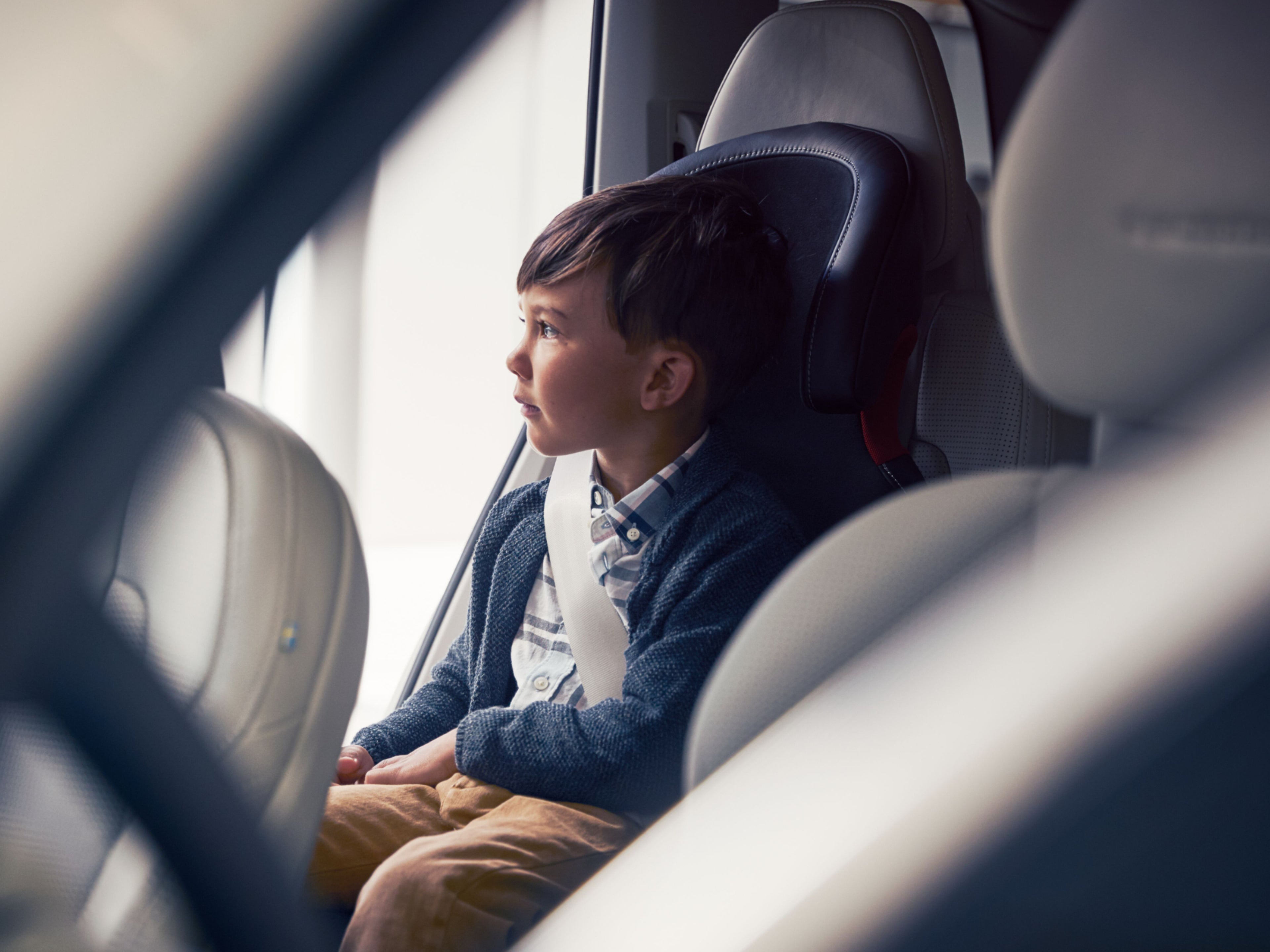 Ein Kind sitzt in einem Kindersitz auf der Rückbank eines Autos und schaut hinaus.