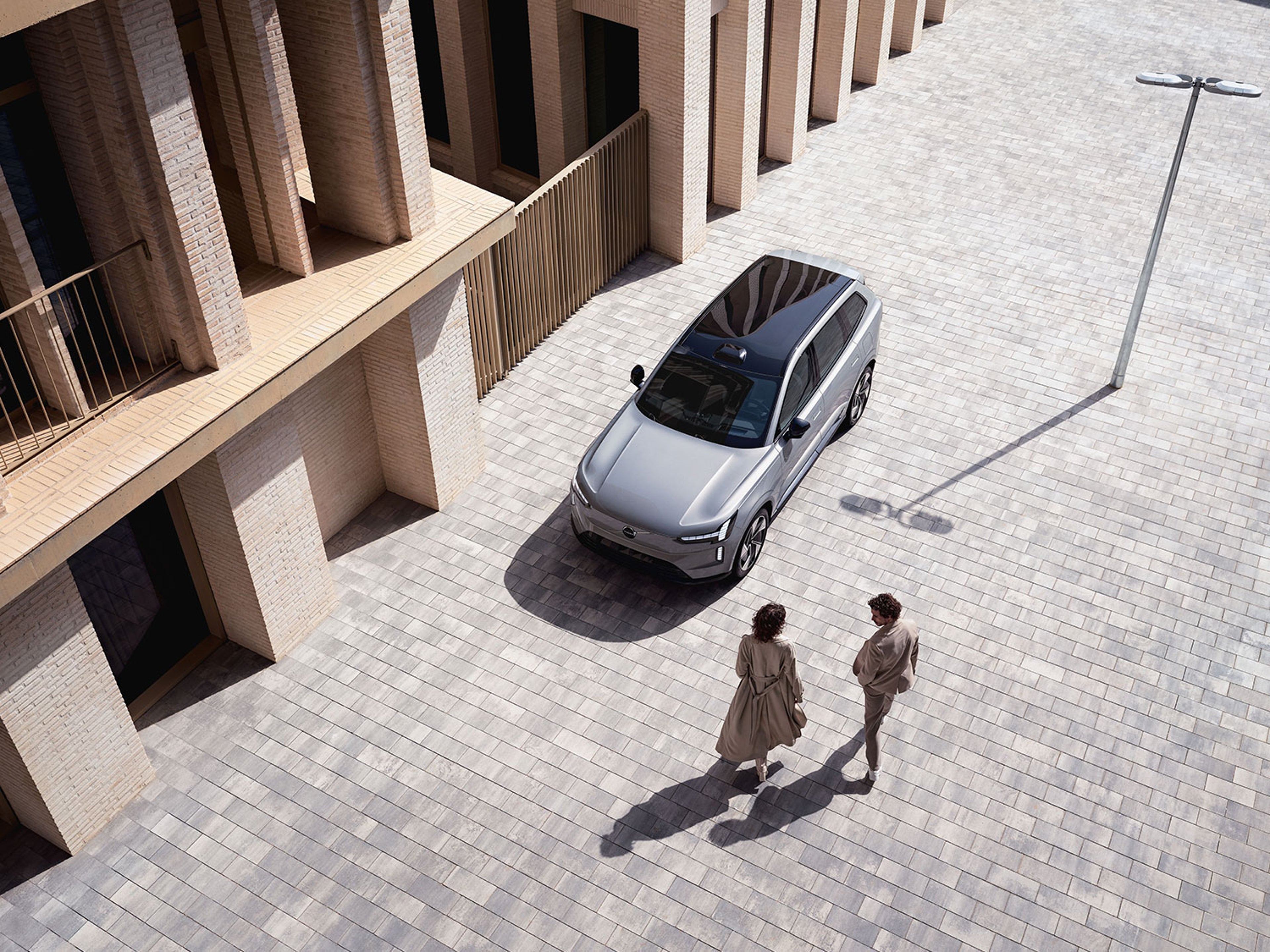 Bovenaanzicht van twee personen die langs een zilvergrijze Volvo EX30 wandelen.