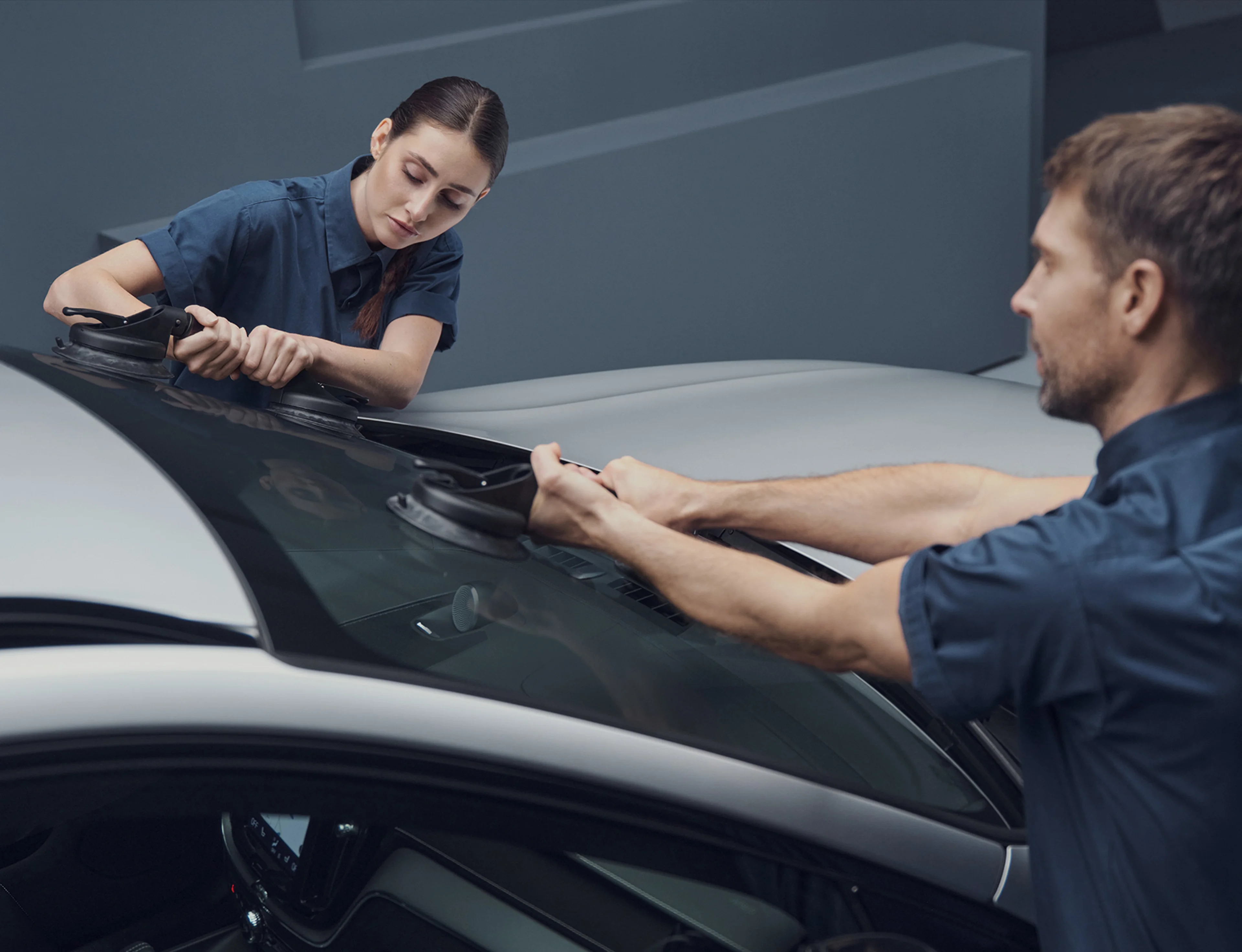 Deux techniciens installent un pare-brise de voiture à l'aide de ventouses.