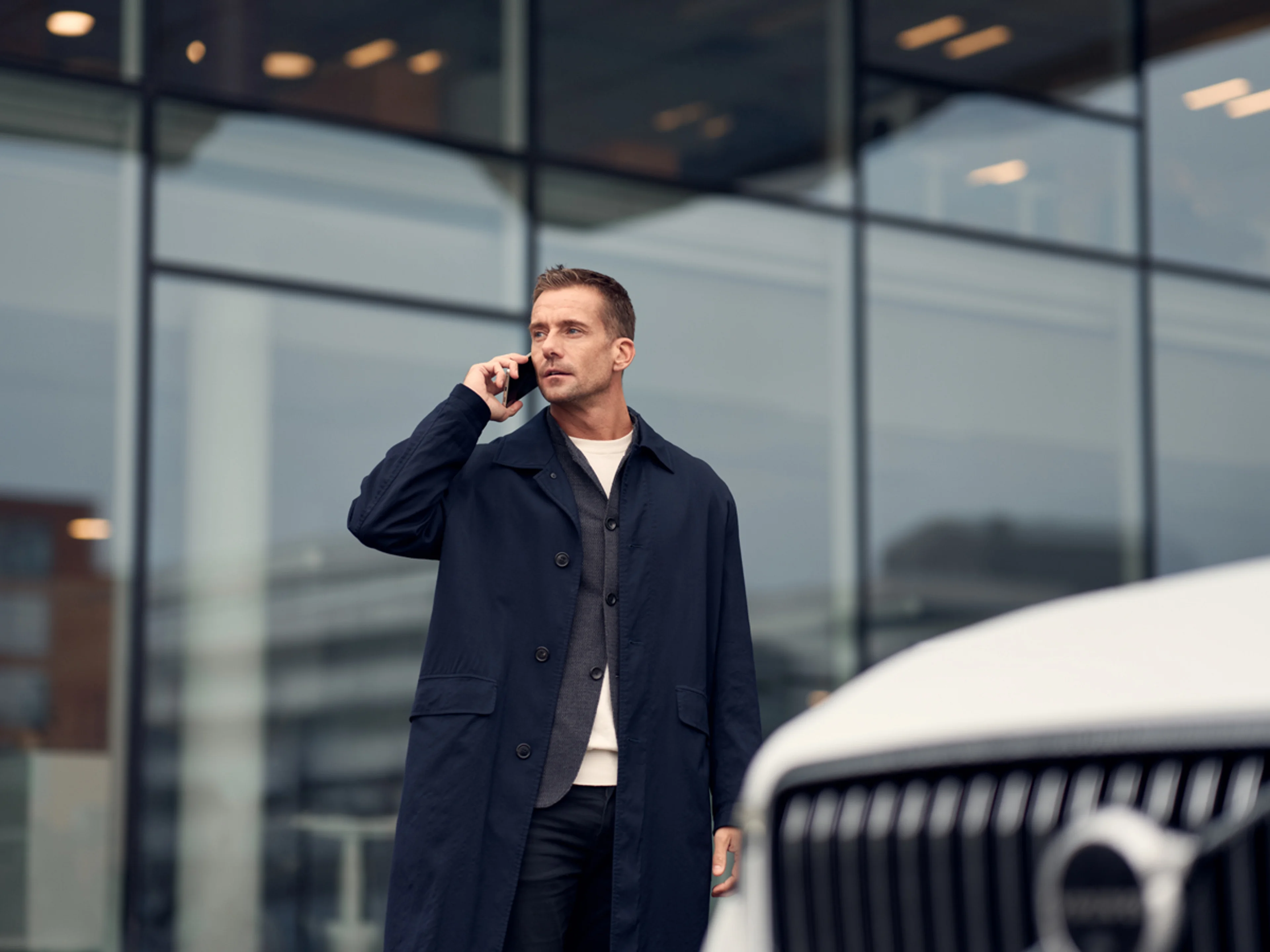 Man pratar i mobil intill en vit Volvo
