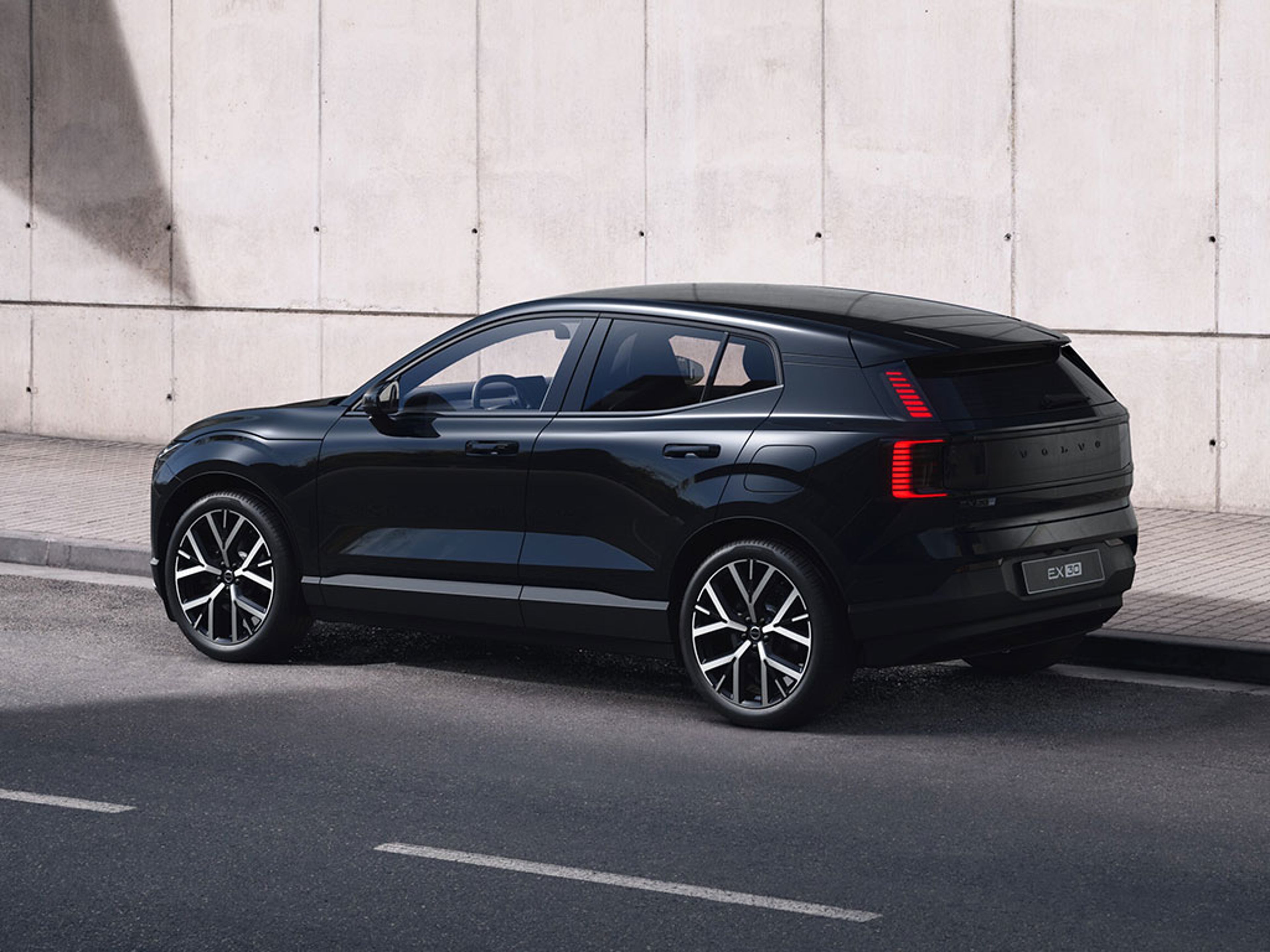 Volvo EX30 Black Edition garé le long d’un mur en béton sous une zone ombragée