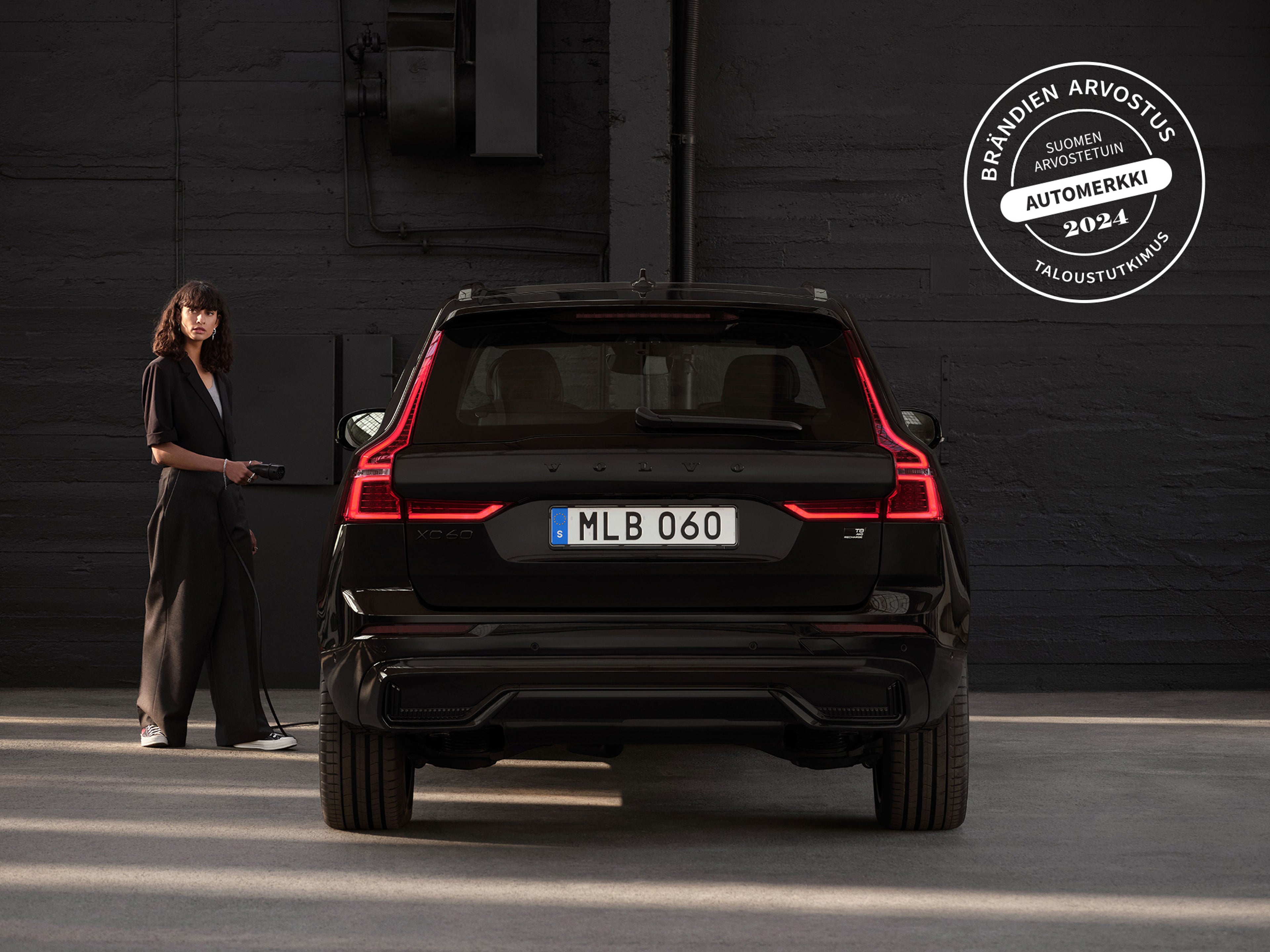 Mustiin pukeutunut nainen ja Volvo XC60 Black Edition -lataushybridi takaa päin kuvattuna.