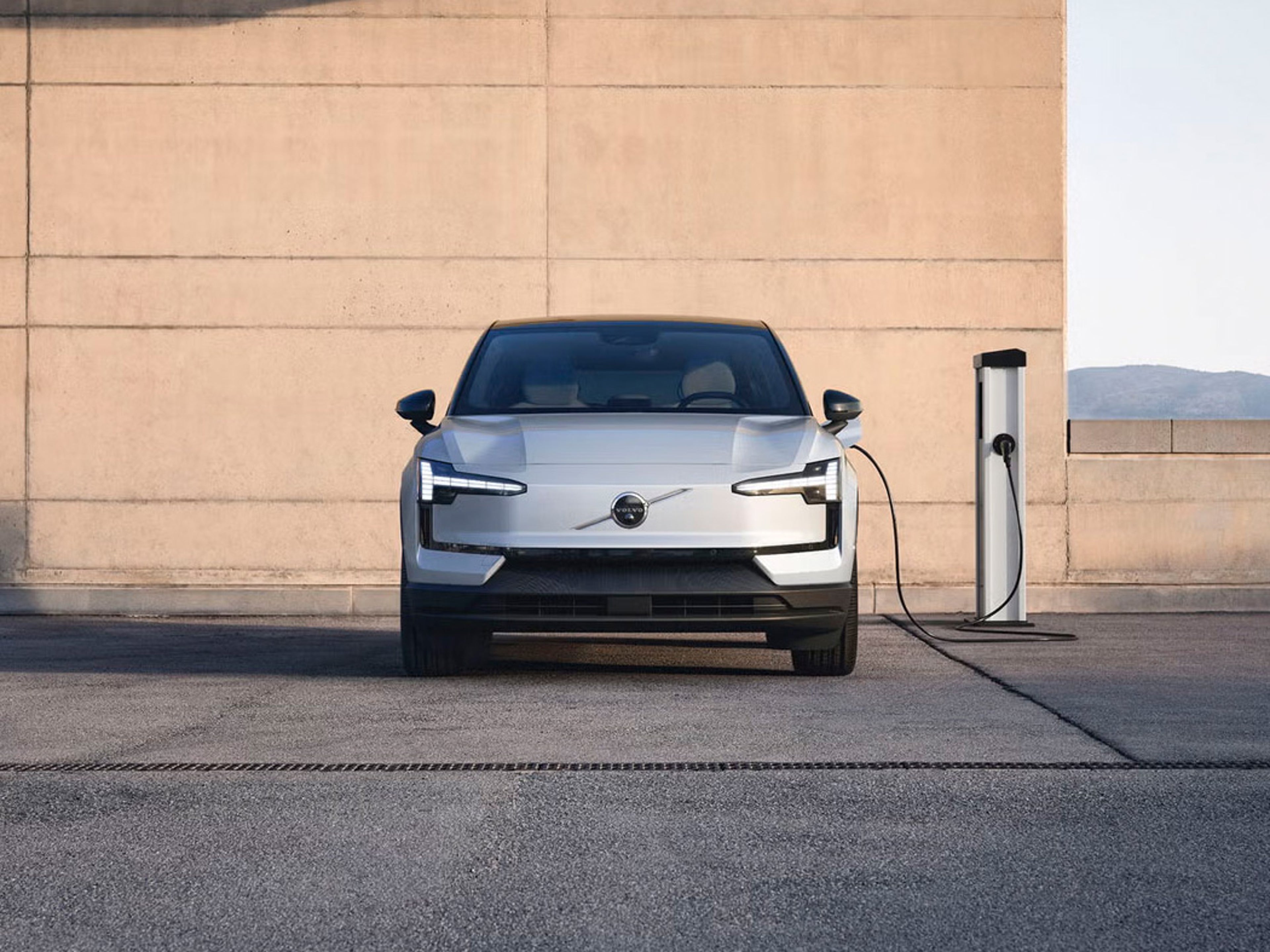 Front view of EX30 plugged into a charger in front of a wall