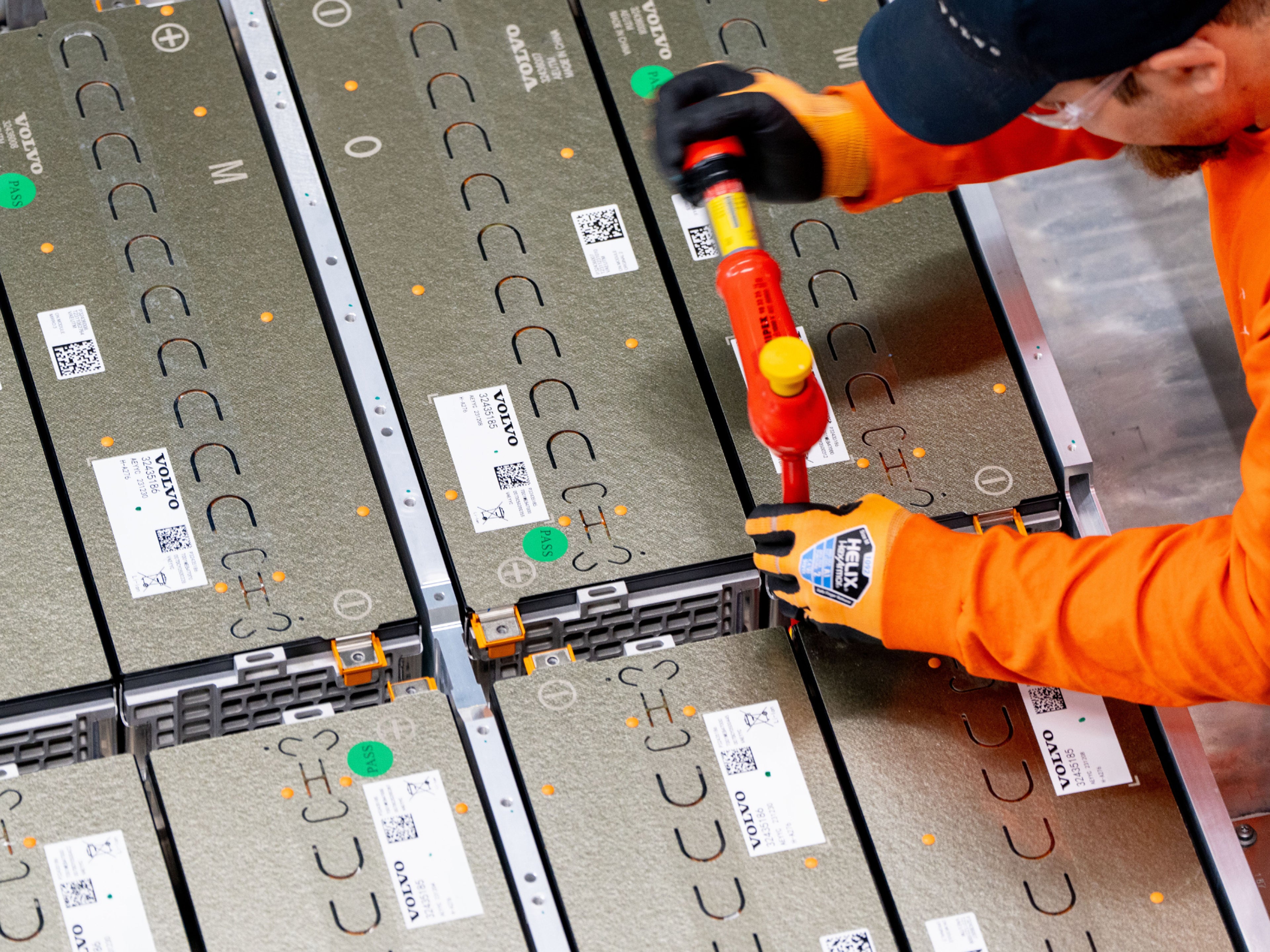 Ein Volvo Mitarbeiter in orangenen Anzug arbeitet an einer Volvo Hochvoltbatterie.