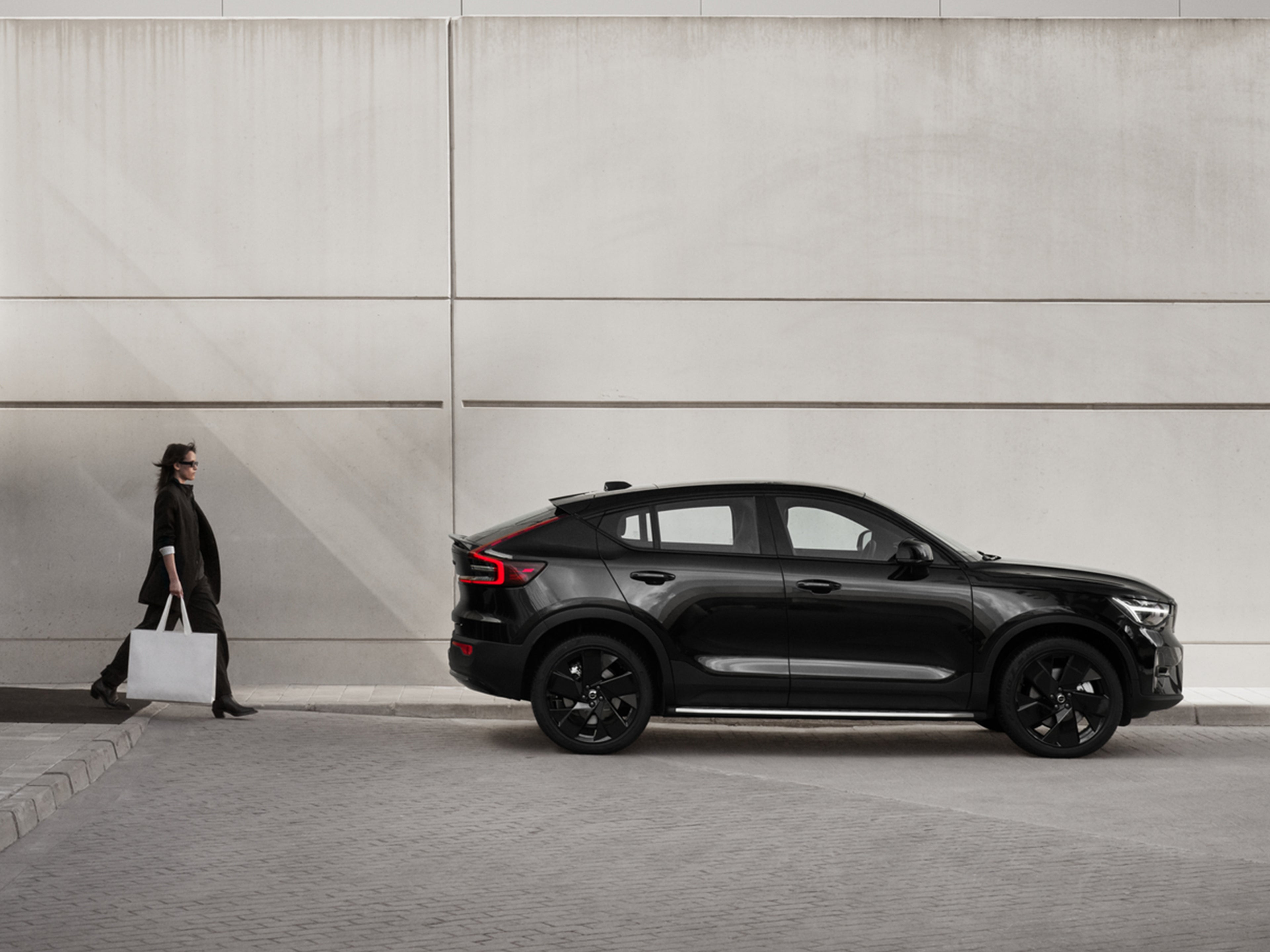 Nainen kävelee kohti pysäköityä Volvo EC40 Black Edition autoa.