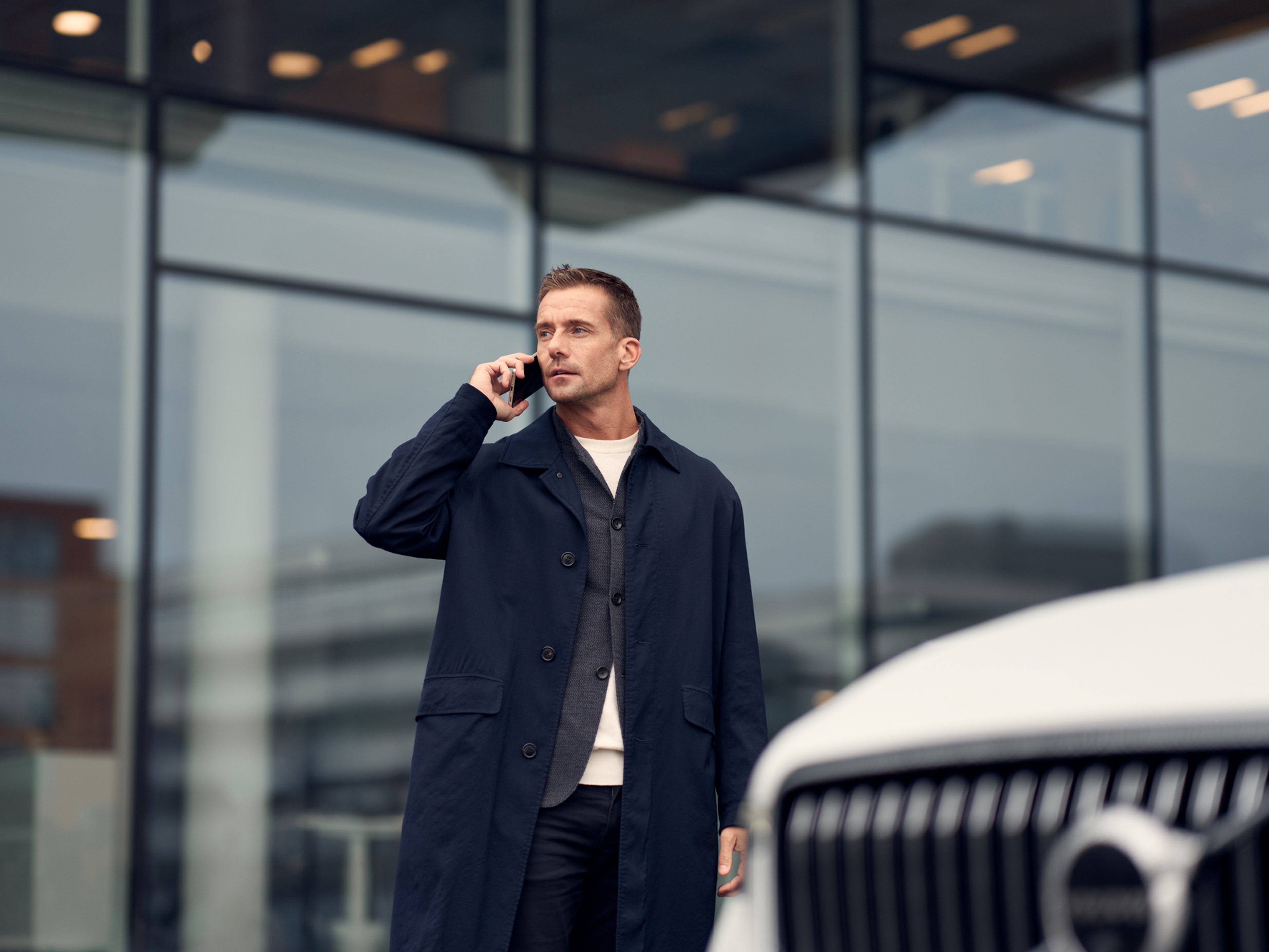 Man talking on the phone with front of white Volvo in foreground