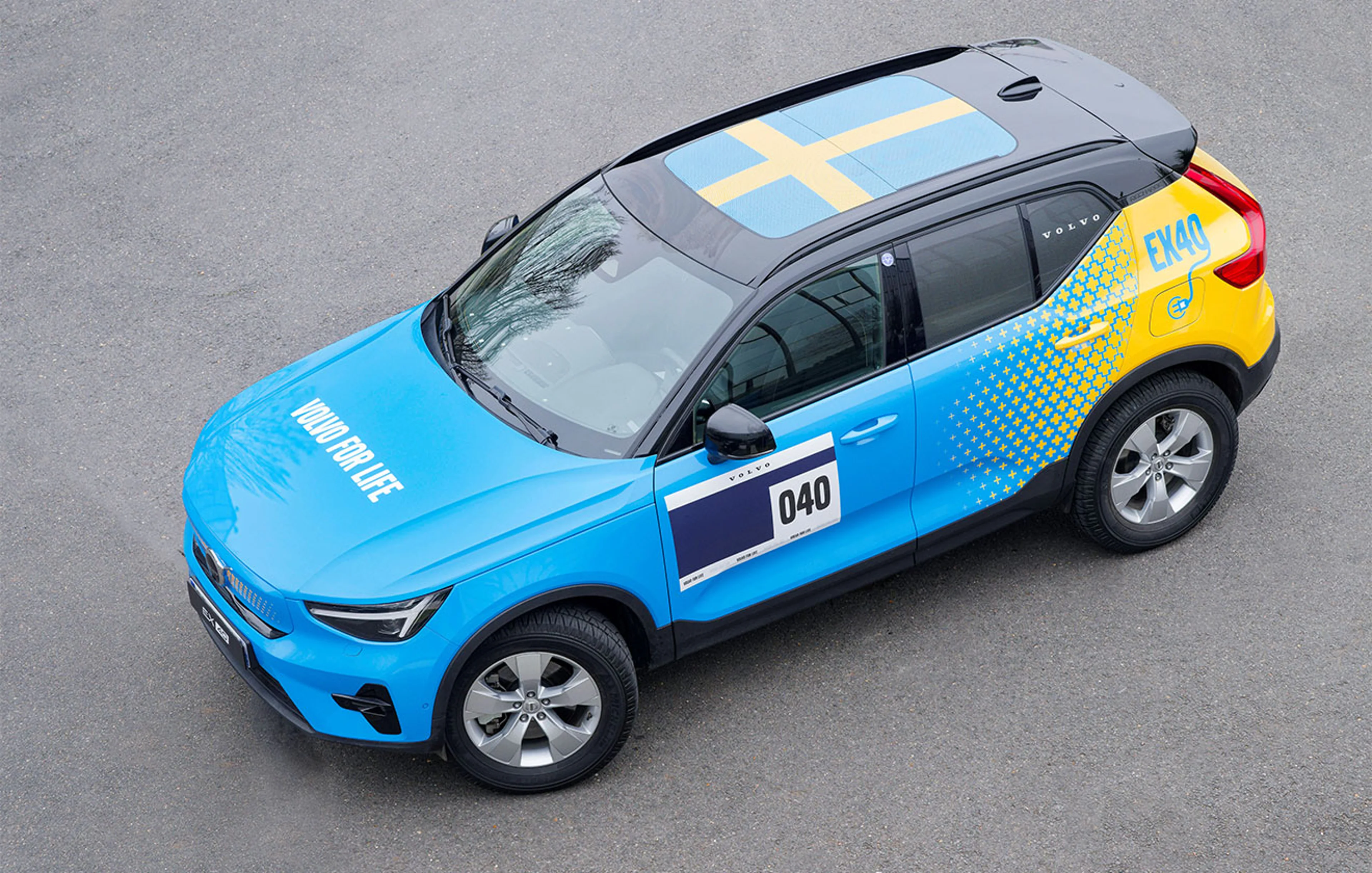 Volvo EX40 bleue et jaune avec drapeau suédois sur le toit, numéro 040 et "Volvo for Life" sur le capot