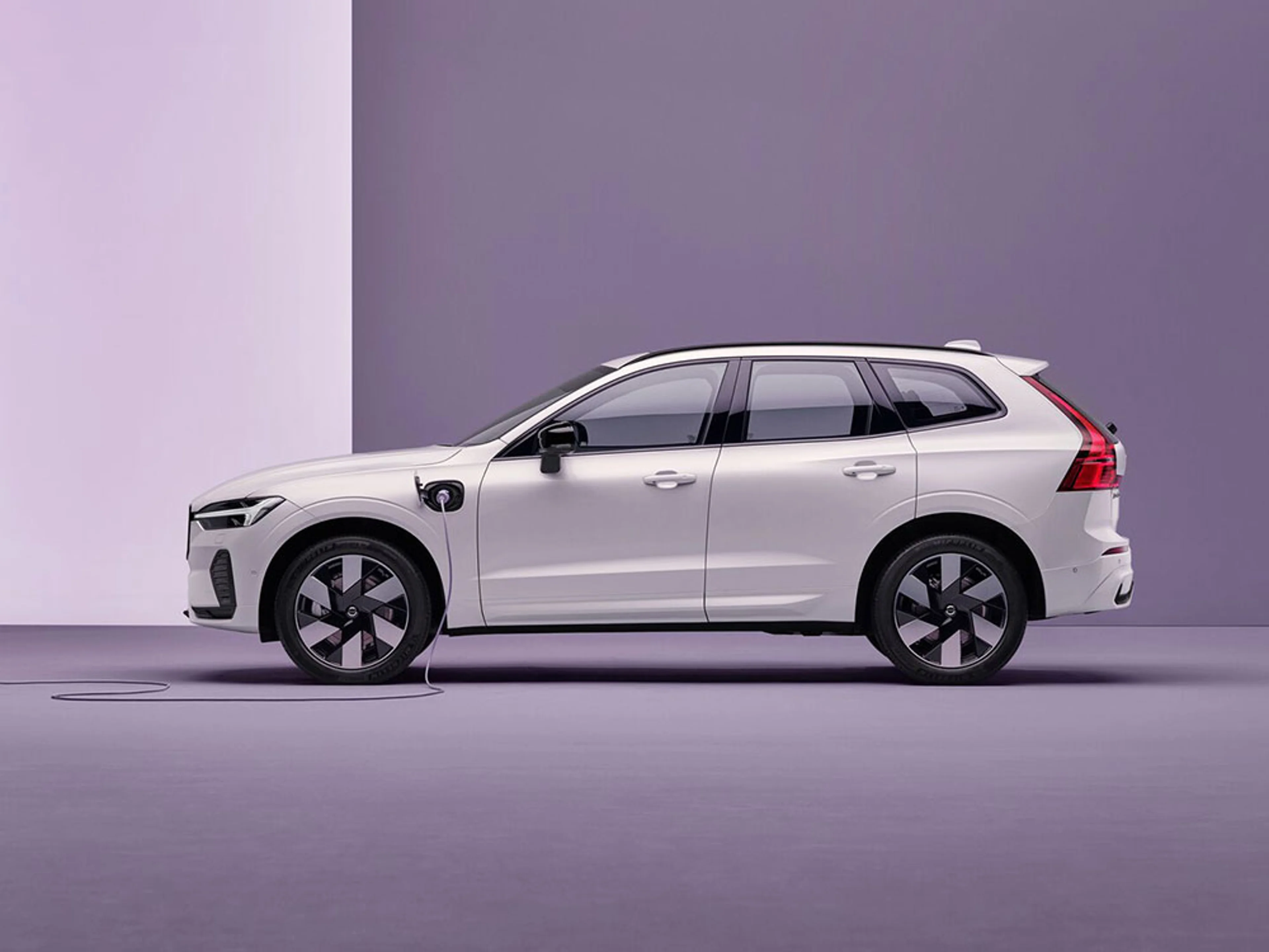 Volvo XC60 blanc branché à une borne de recharge sur fond violet