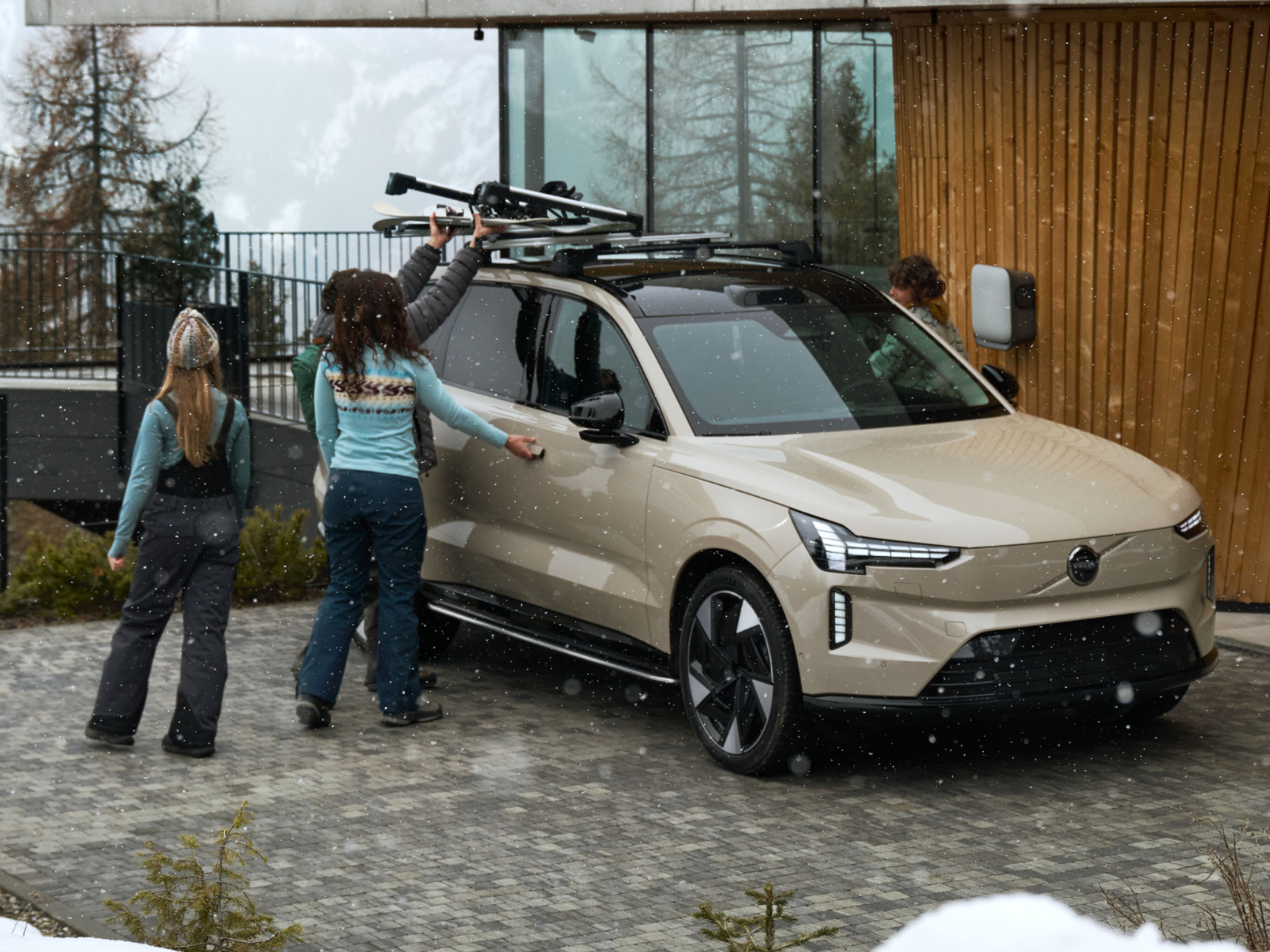 Drei Personen befestigen Skier auf dem schwarzen Dach eines Volvo EX90.