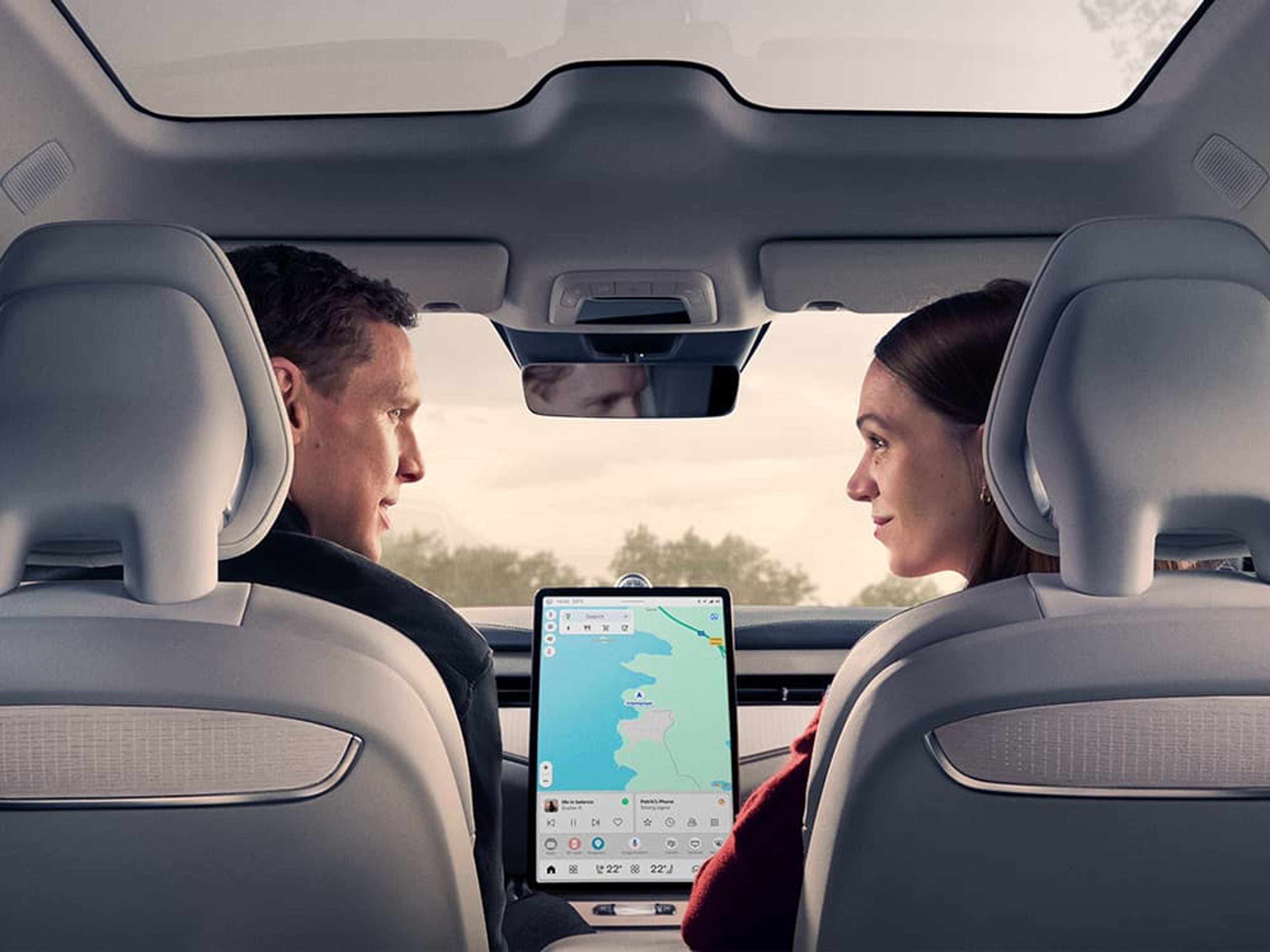 Un homme et une femme sont assis dans une Volvo ES90 avec un toit panoramique et regardent la tablette sur le tableau de bord.